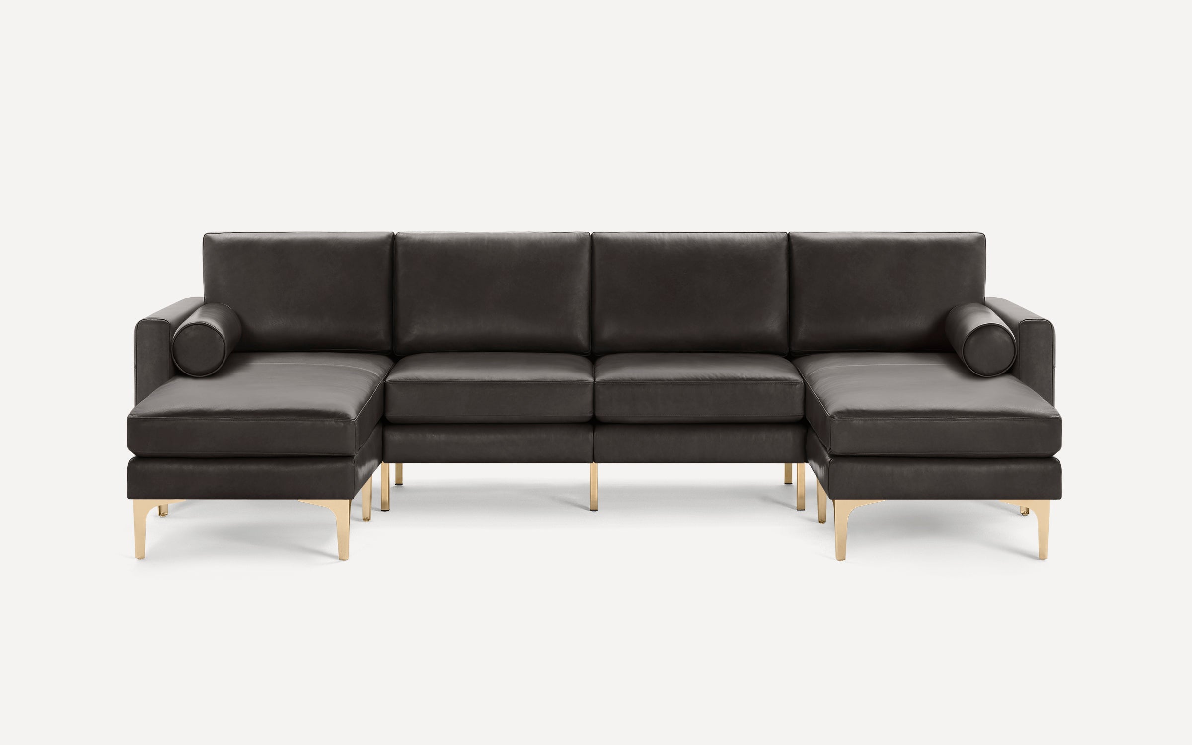 Modern dark gray leather sectional sofa with gold metal legs and two cylindrical bolster pillows.