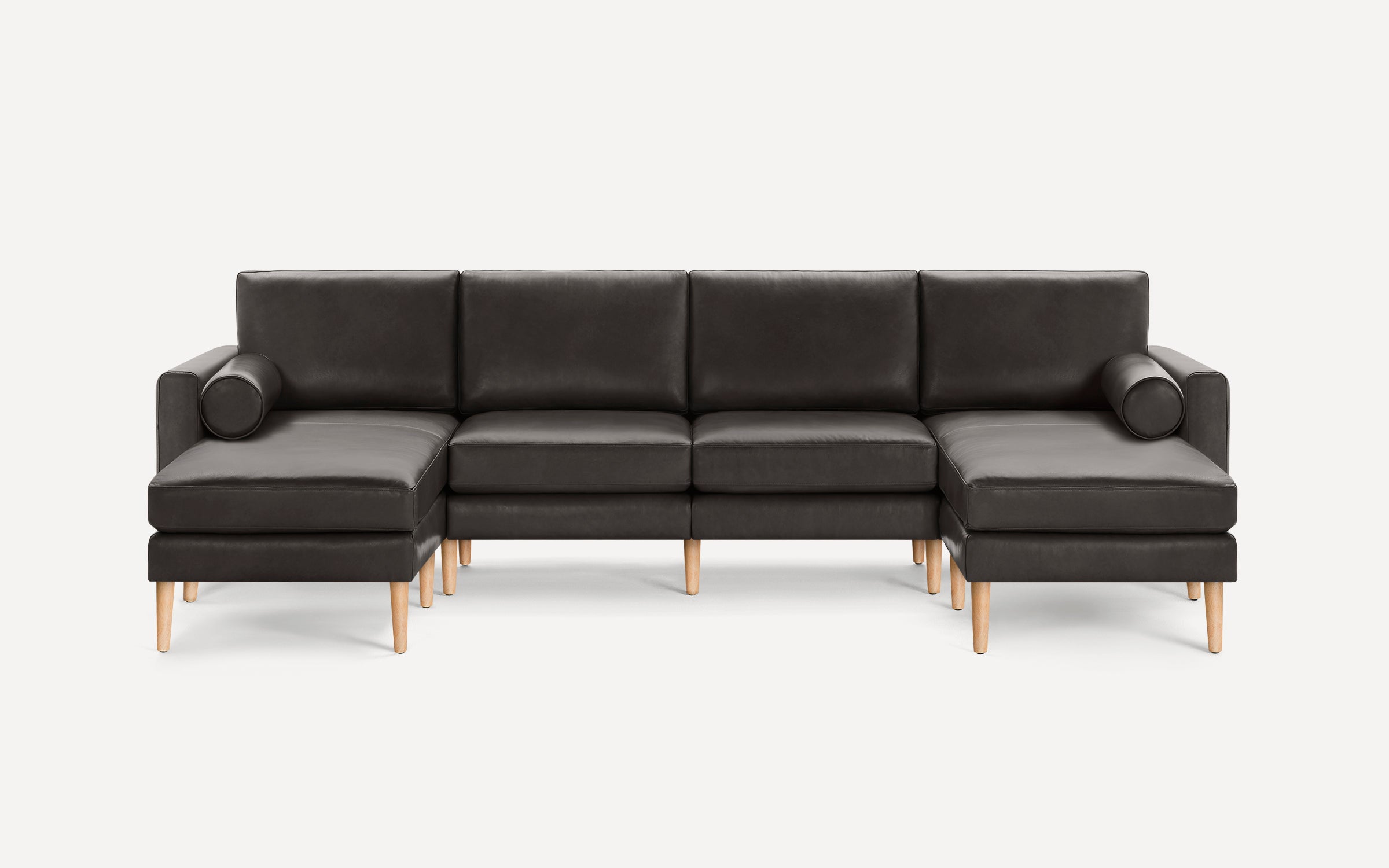 Dark gray leather U-shaped sectional sofa with wooden legs and cylindrical bolster pillows on both ends.