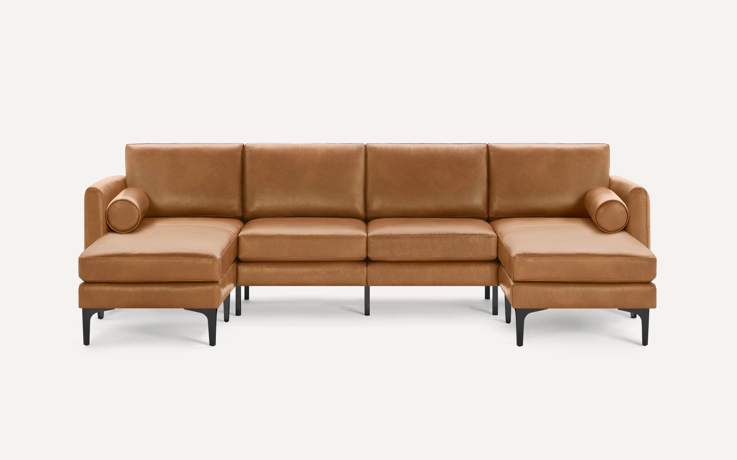 Modern tan leather sectional sofa with black metal legs, featuring two chaise lounges and cylindrical bolster pillows on each end.