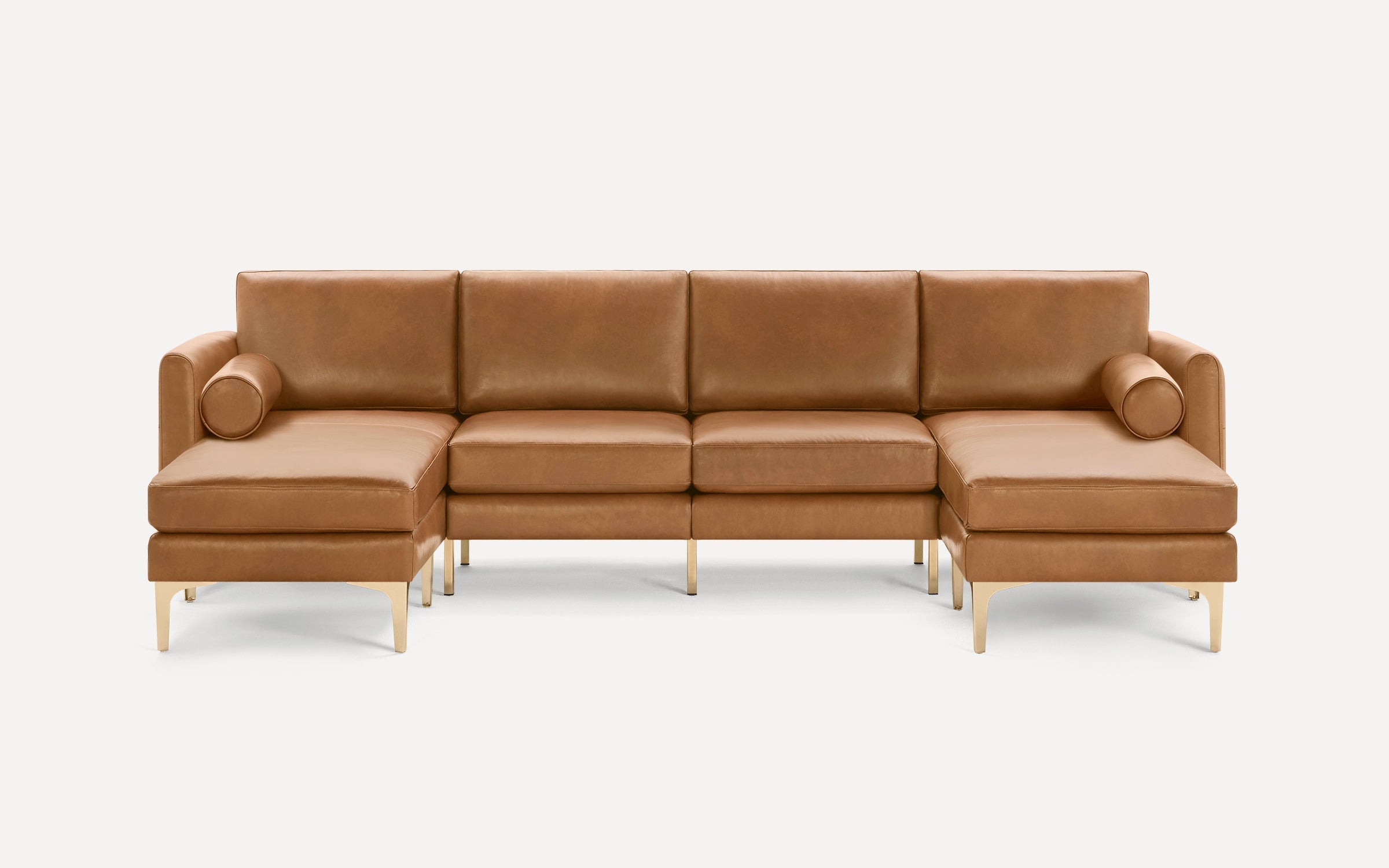 Modern brown leather sectional sofa with gold-toned metal legs, featuring two bolster pillows on each end for added comfort.