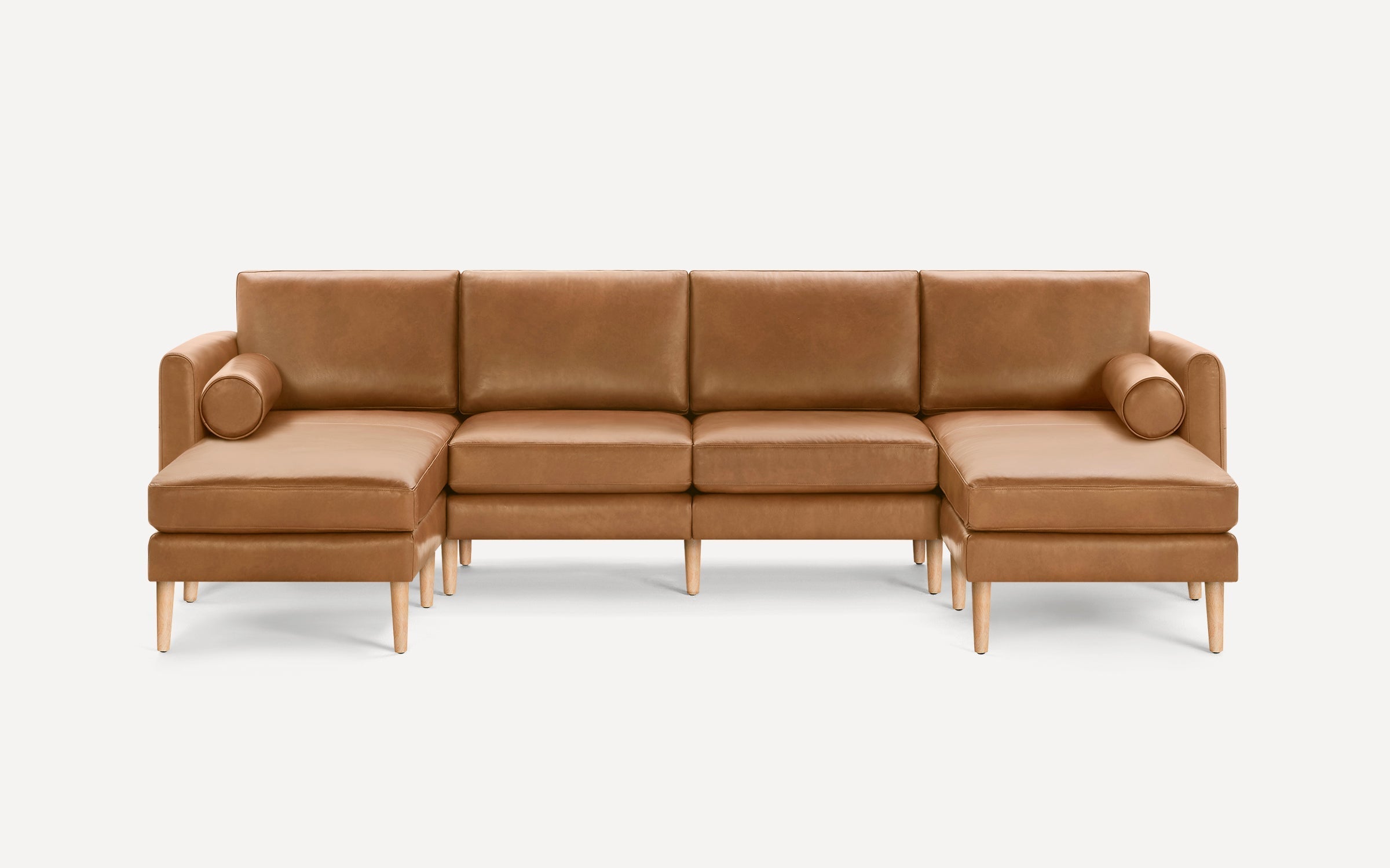 Modern mid-century style tan leather sectional sofa with wooden legs and cylindrical bolster pillows on each side.