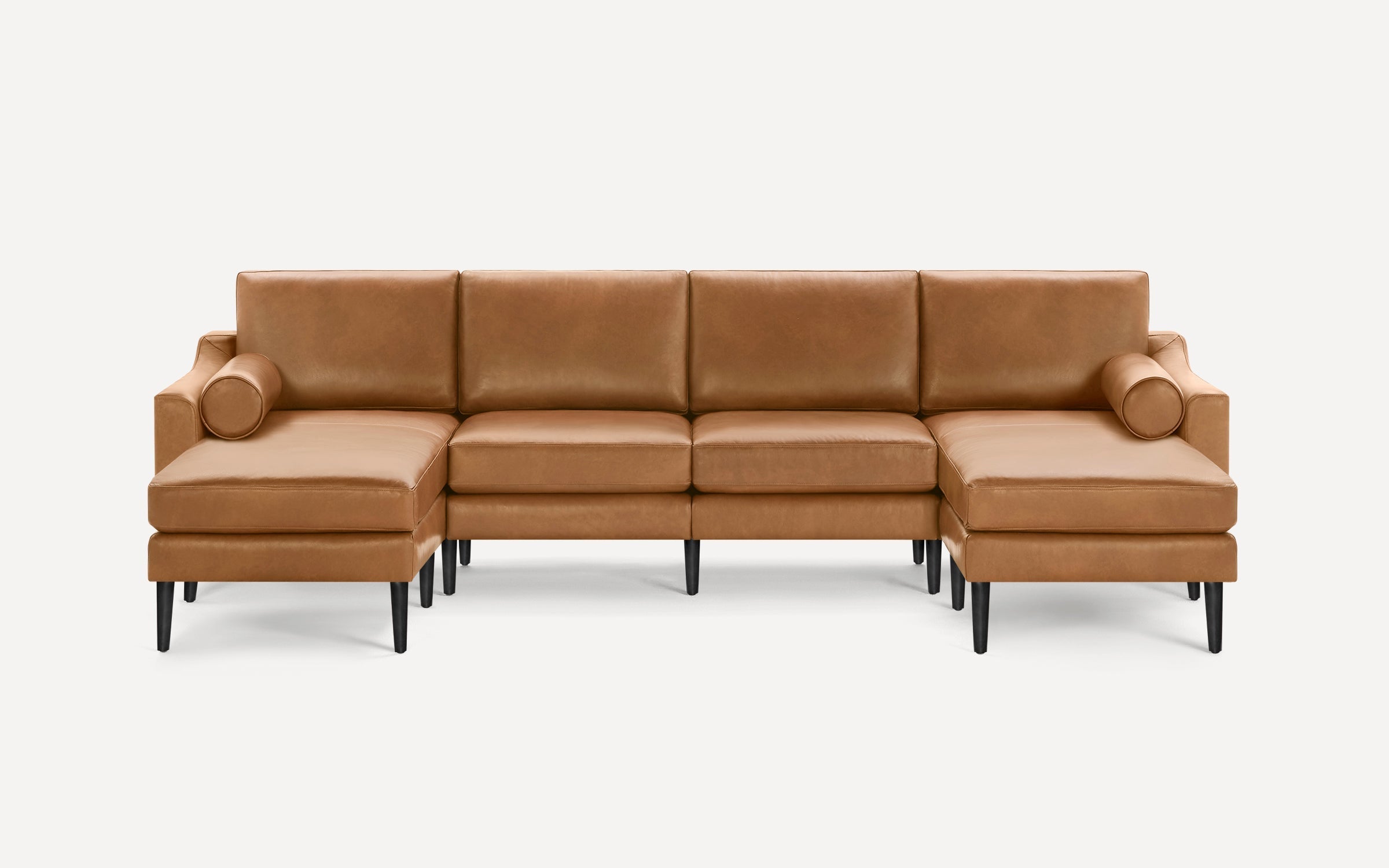Modern U-shaped sectional sofa in light brown leather with cylindrical bolster pillows, black tapered legs, and clean lines on a white background.