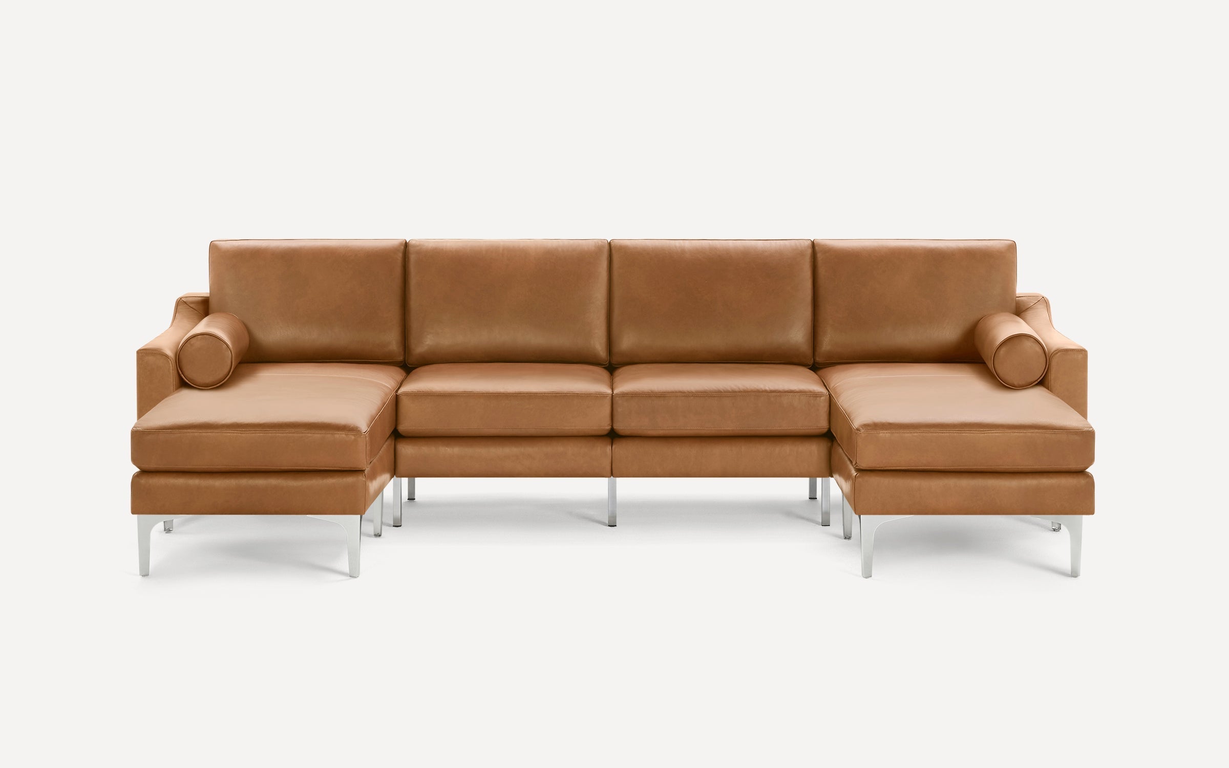 Modern tan leather sectional sofa with clean lines, chrome legs, and two cylindrical bolster pillows on each end.