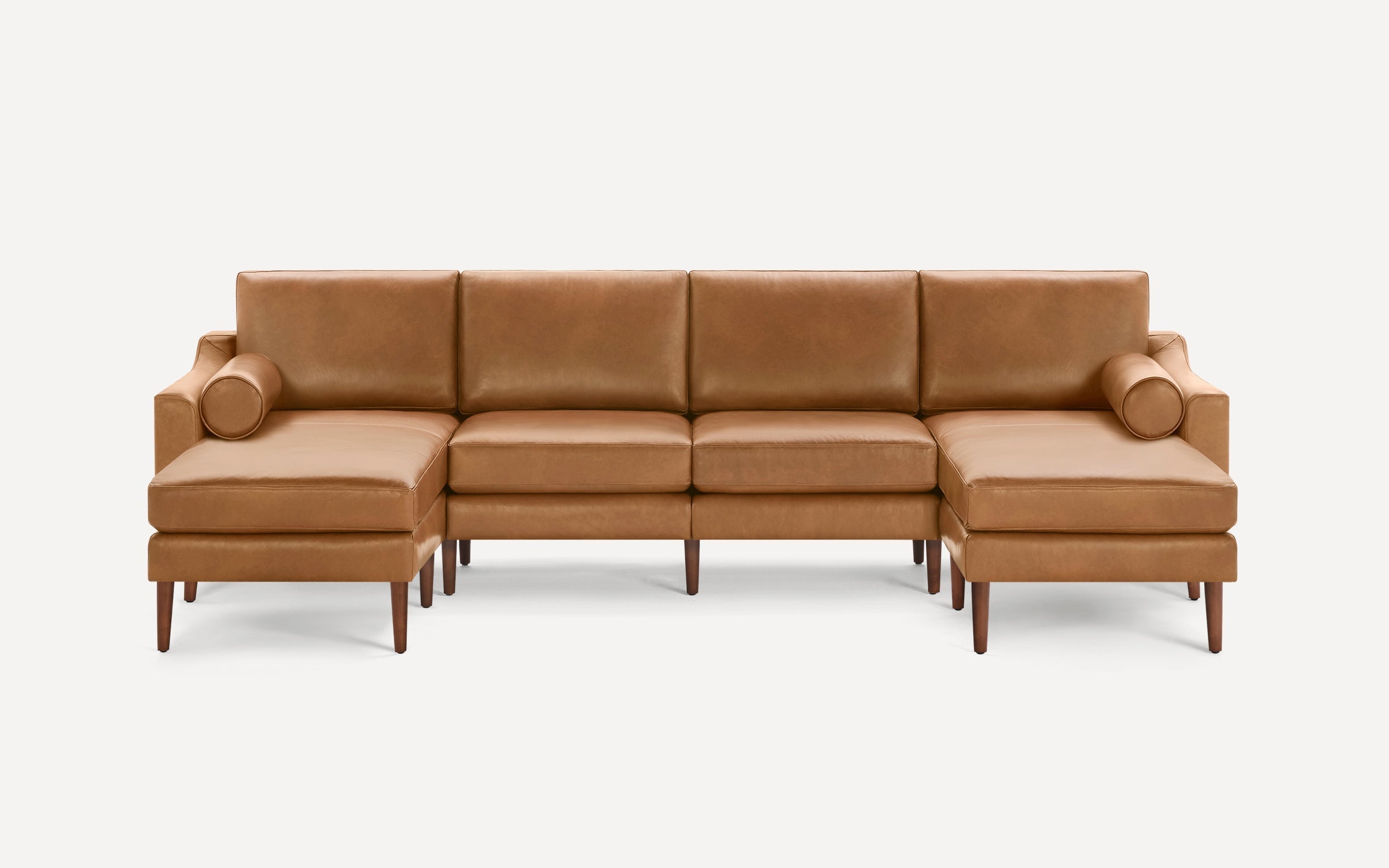 Mid-century modern tan leather sectional sofa with straight wooden legs, two bolster pillows, and clean lines on a white background.