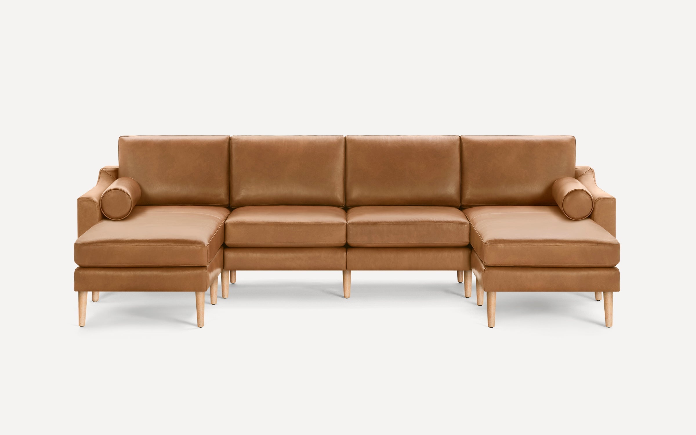 Modern tan leather sectional sofa with wooden legs, featuring two chaise lounges and cylindrical bolster pillows on each end.