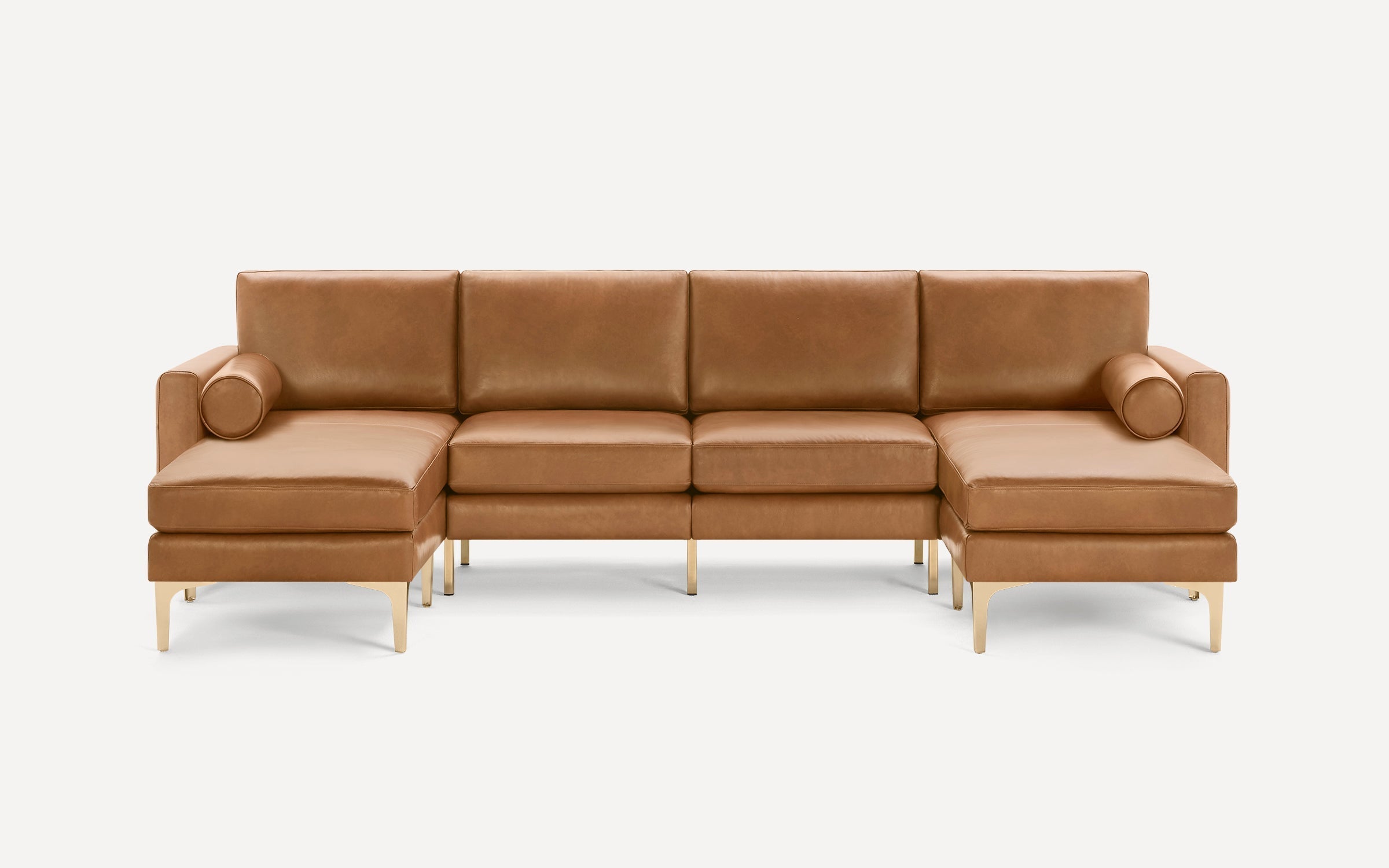 Modern L-shaped tan leather sectional sofa with gold metal legs and two cylindrical bolster pillows on each end.