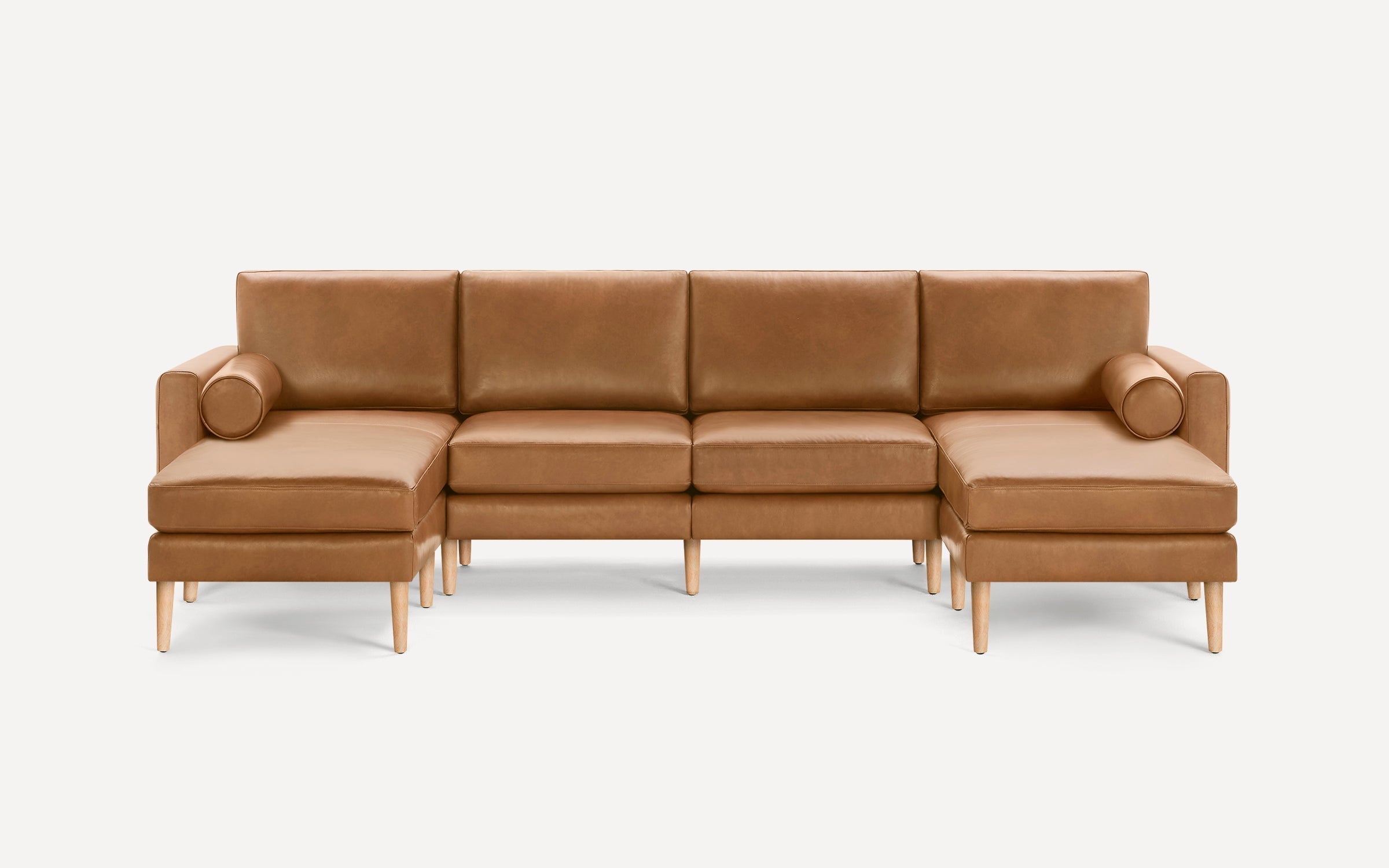 Mid-century modern tan leather sectional sofa with wooden legs, two bolster pillows, and clean, straight lines.