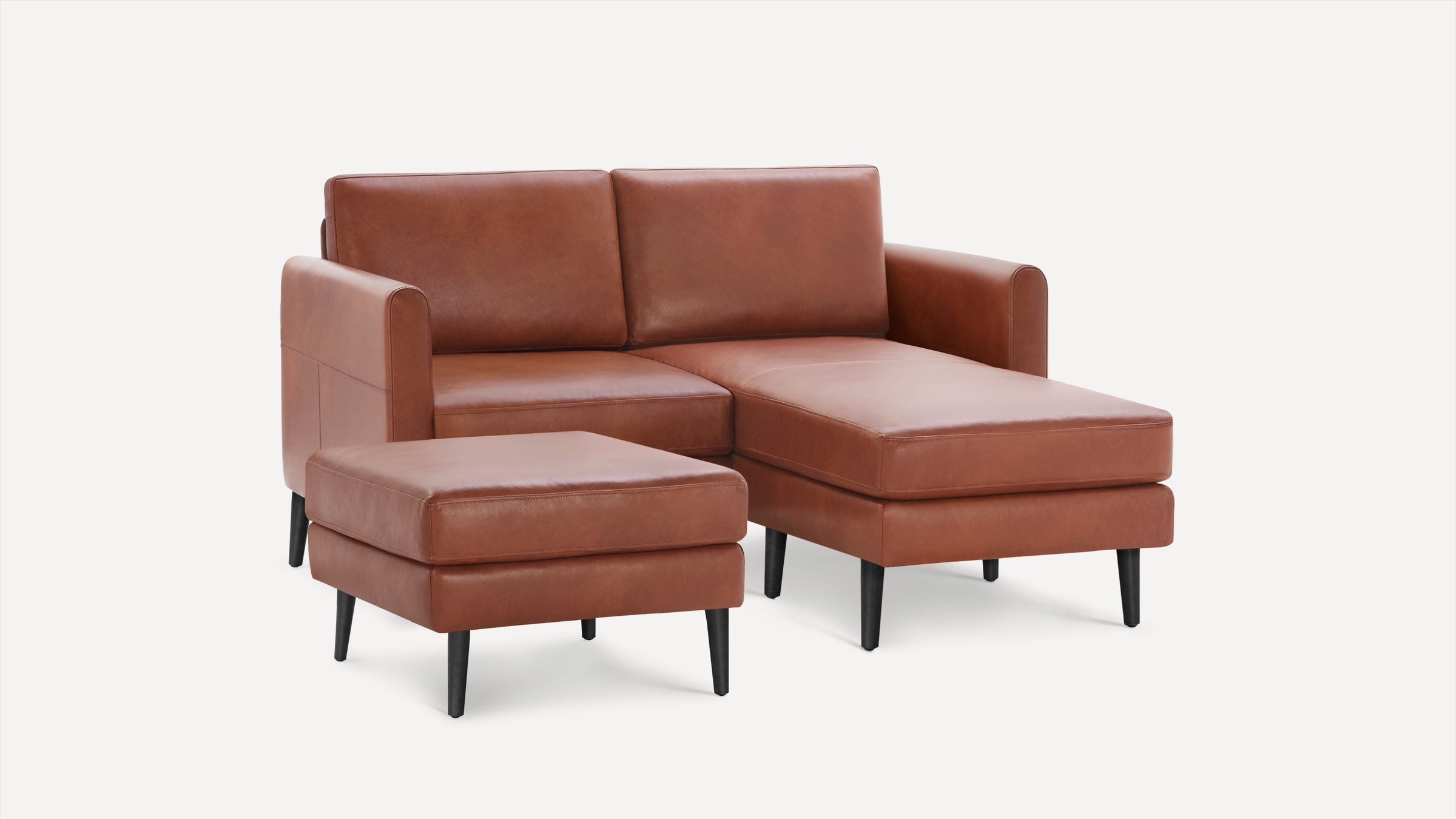 Brown leather sectional sofa with chaise lounge and separate ottoman, featuring black tapered legs and modern design.