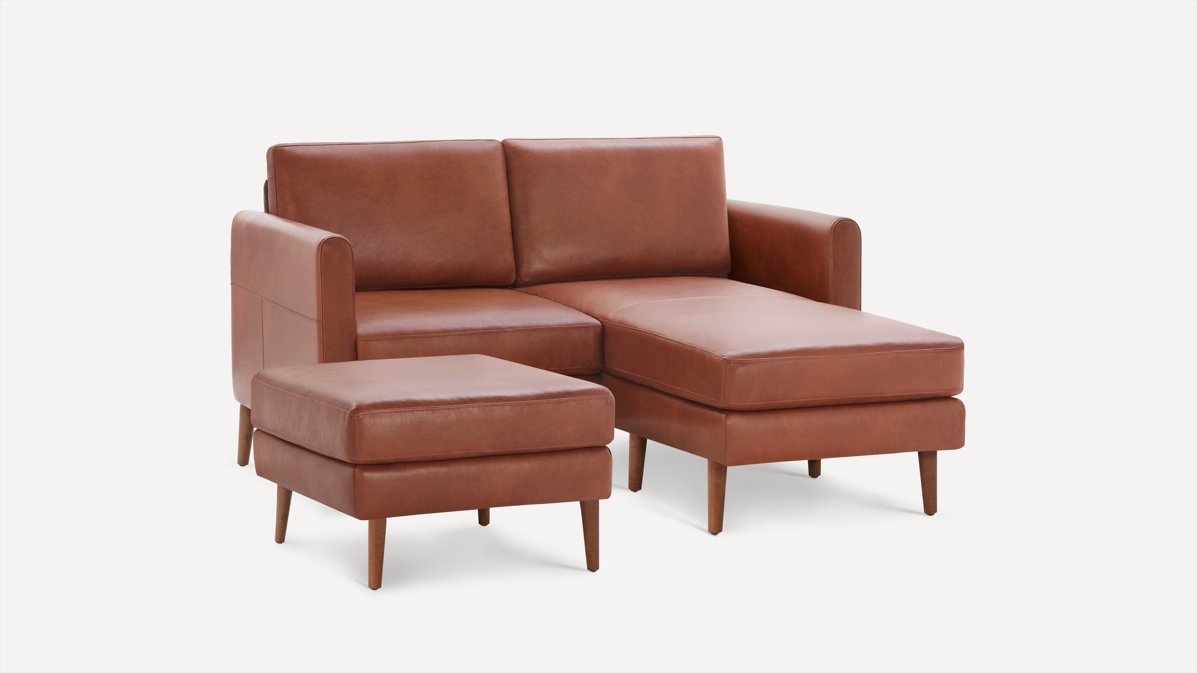 Mid-century modern style brown leather chaise sofa with matching ottoman, tapered wooden legs, and clean lines.