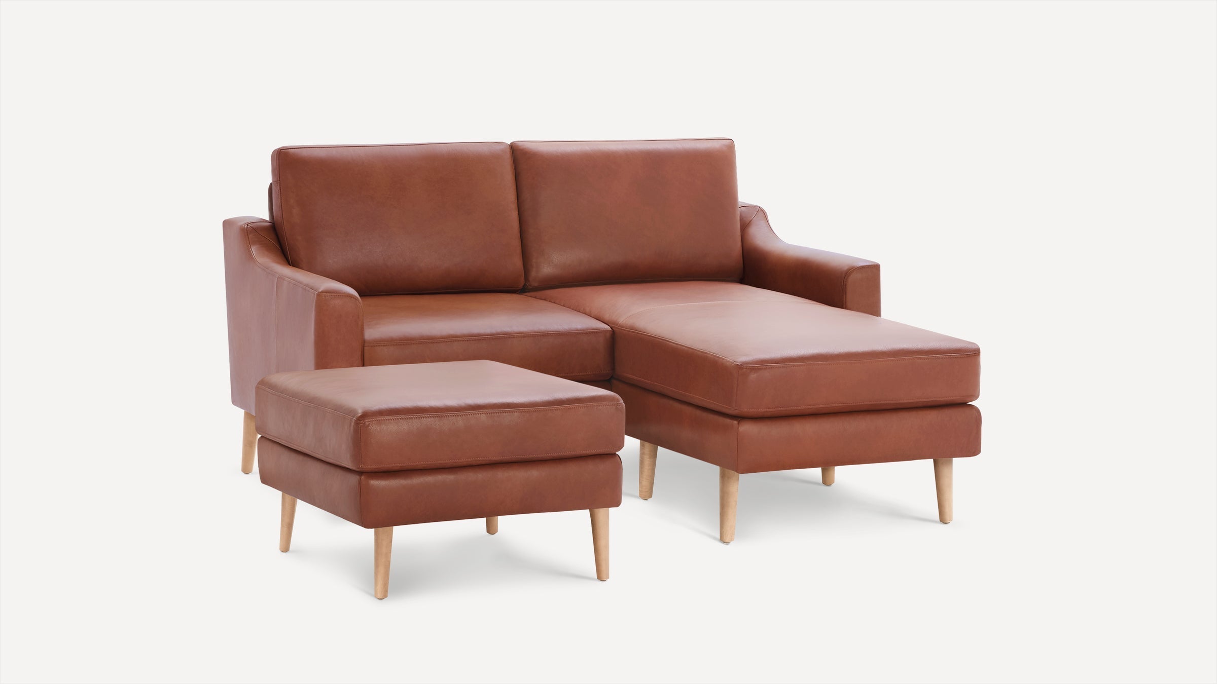 Brown leather sectional sofa with a chaise lounge on the right and matching ottoman, wooden tapered legs.