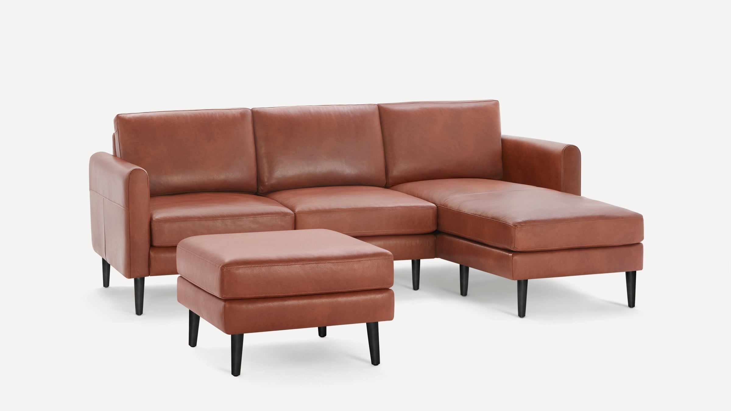 Brown leather sectional sofa with chaise lounge and matching square ottoman, supported by black tapered legs.