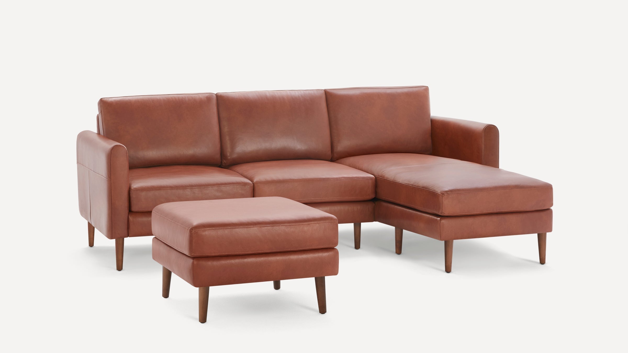 Mid-century style brown leather sectional sofa with chaise lounge and matching ottoman, supported by tapered wooden legs.