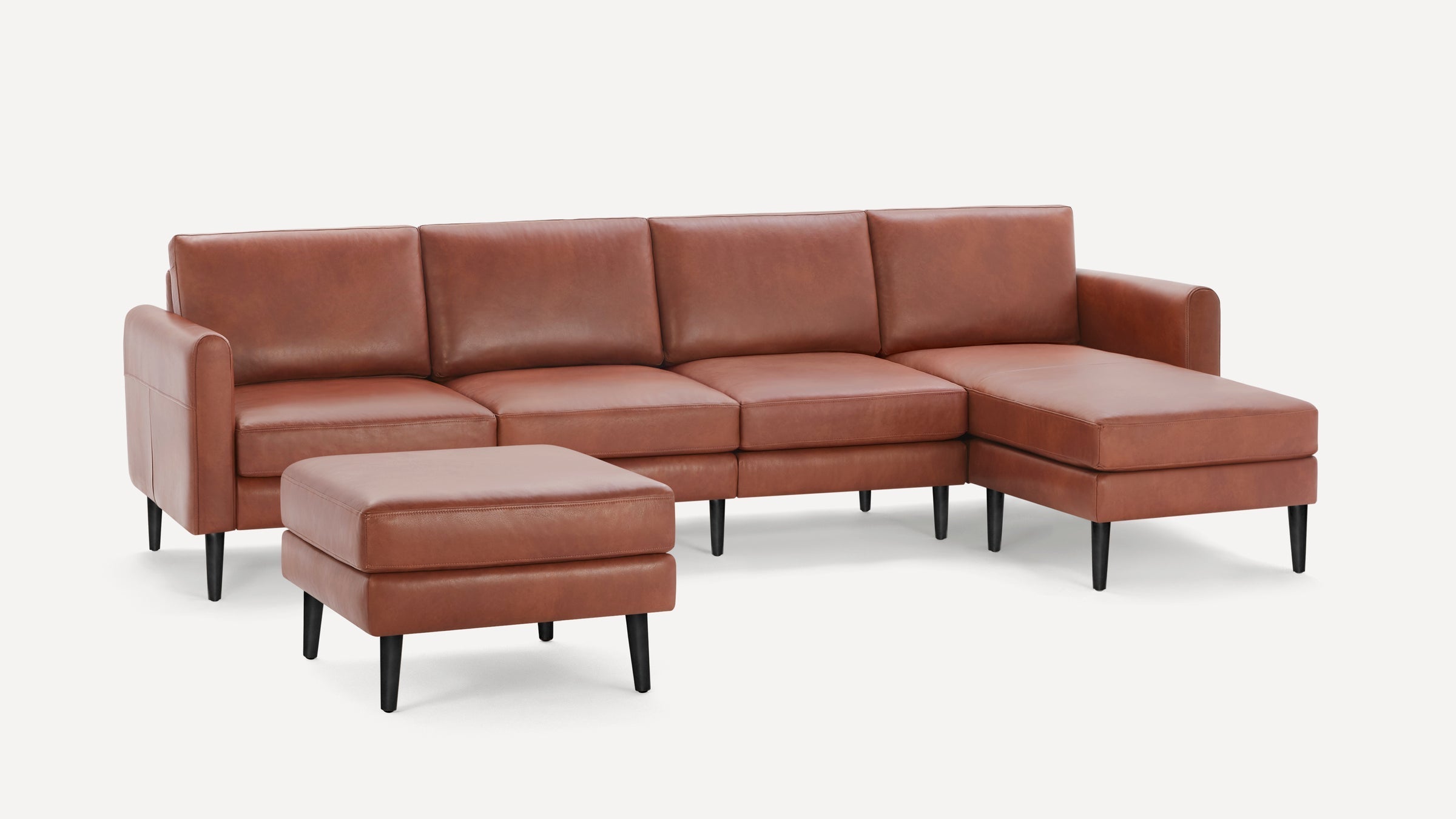 Brown leather sectional sofa with chaise lounge and matching ottoman, featuring sleek black legs and modern design.