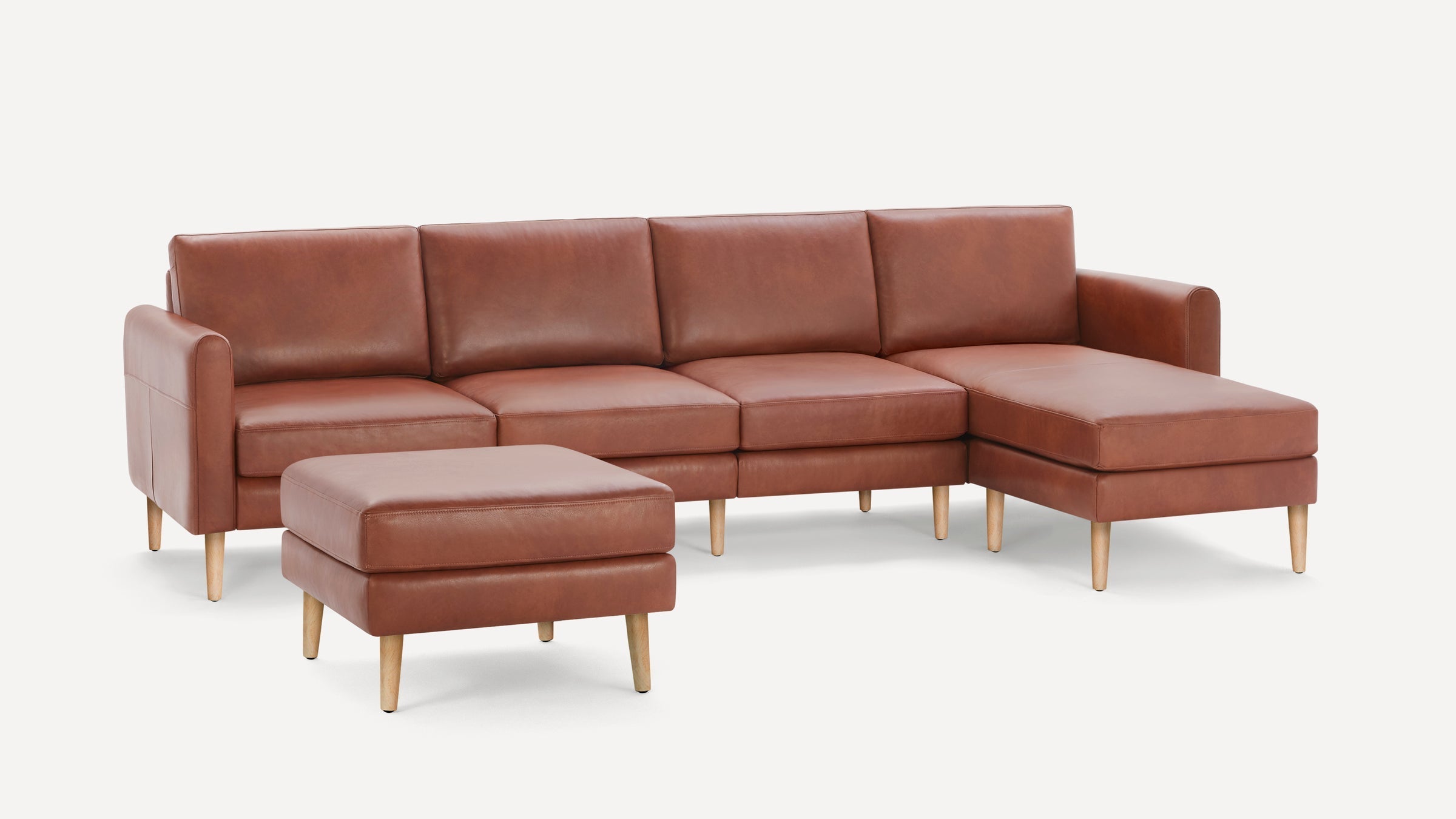 Mid-century modern brown leather sectional sofa with a chaise lounge and matching ottoman, featuring wooden legs.