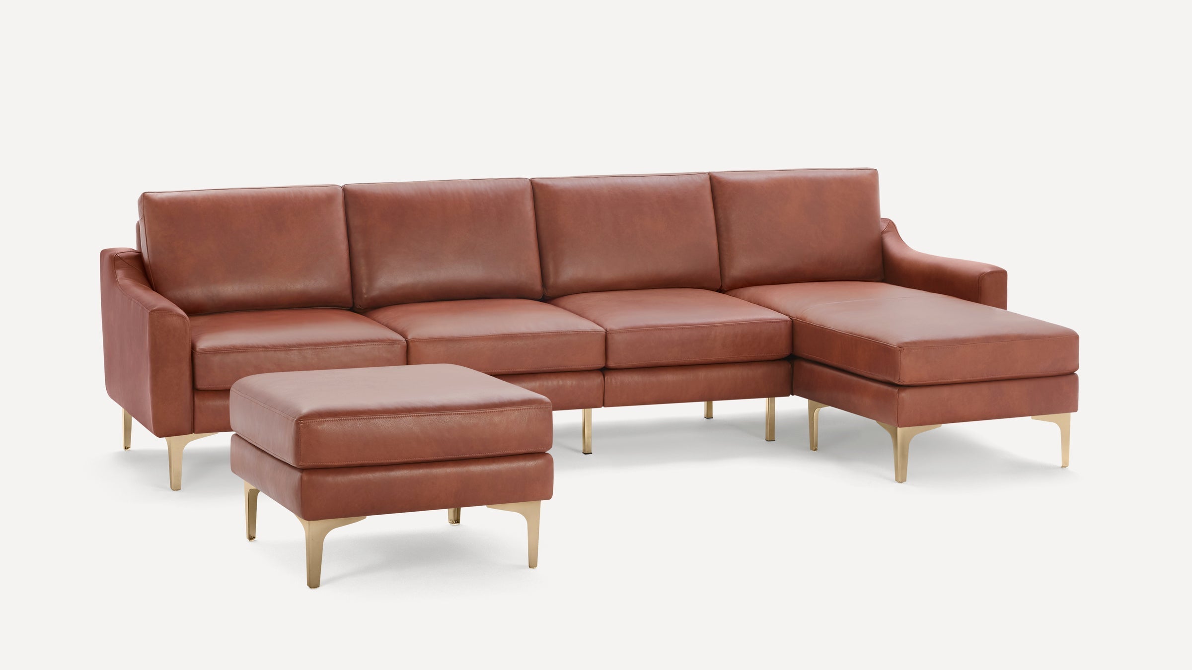 Brown leather sectional sofa with chaise lounge and matching ottoman, featuring gold metal legs on a white background.