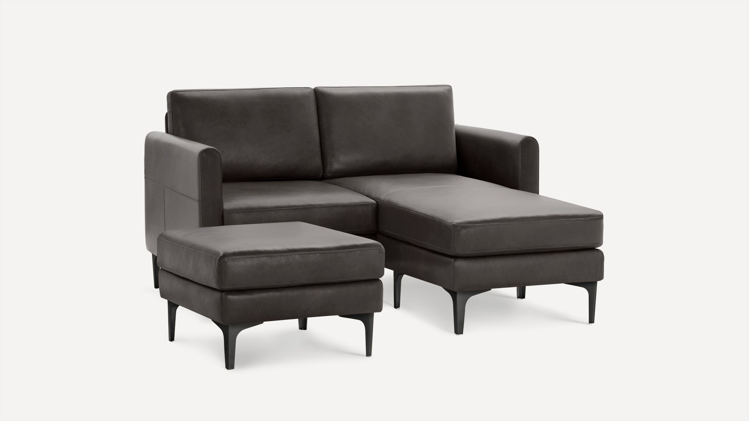 Dark gray leather sectional sofa with chaise lounge and matching ottoman on black tapered legs against white background.