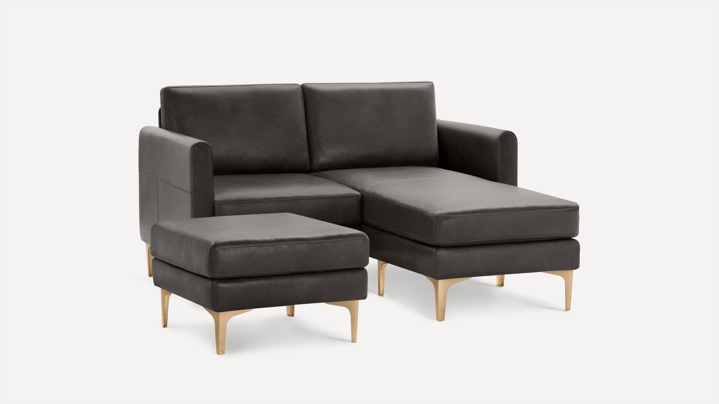 Modern dark gray leather sectional sofa with a matching ottoman, featuring sleek gold-toned metal legs.