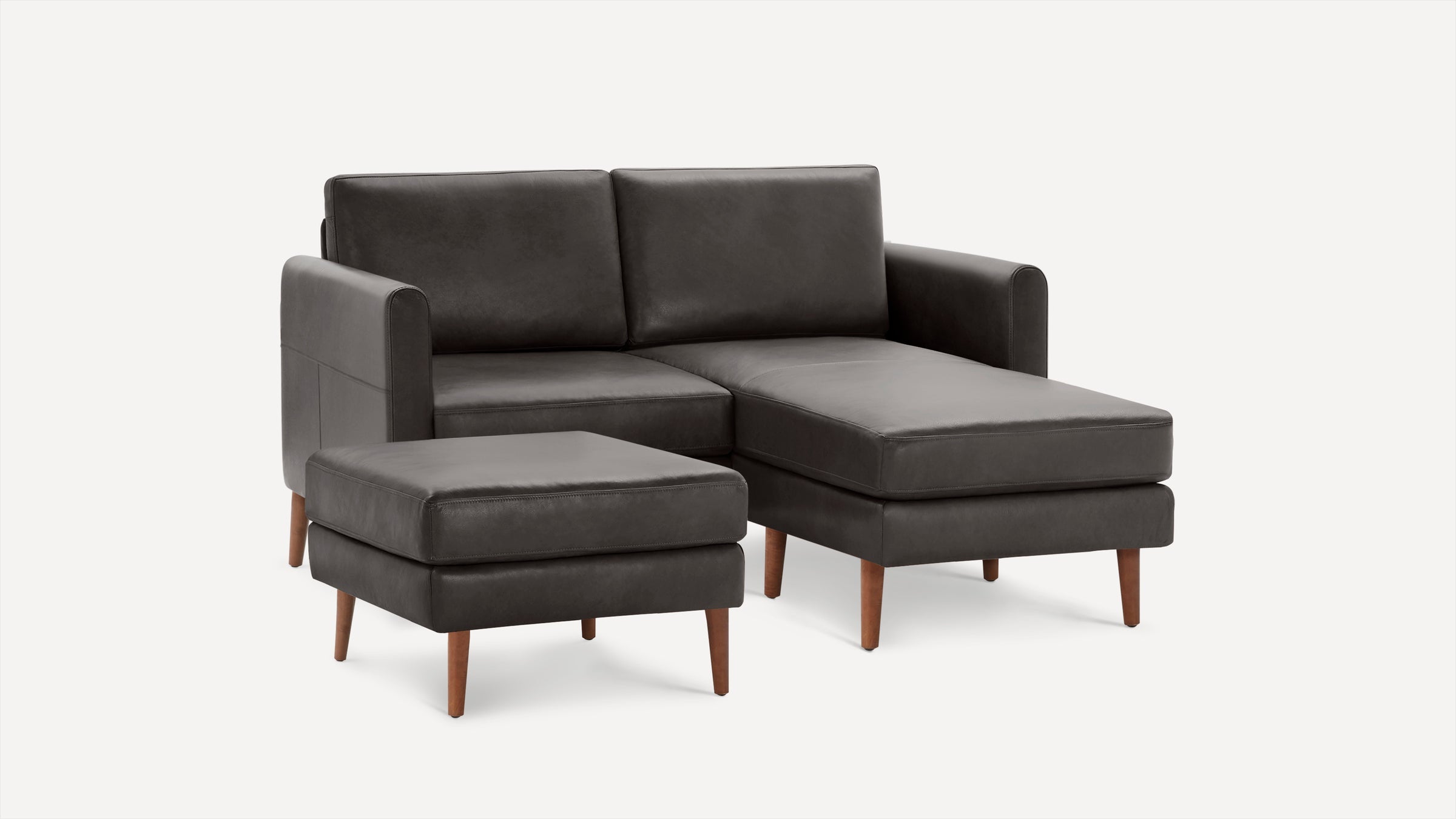 Dark gray leather sectional sofa with matching ottoman, wooden legs, and modern clean lines on a white background.