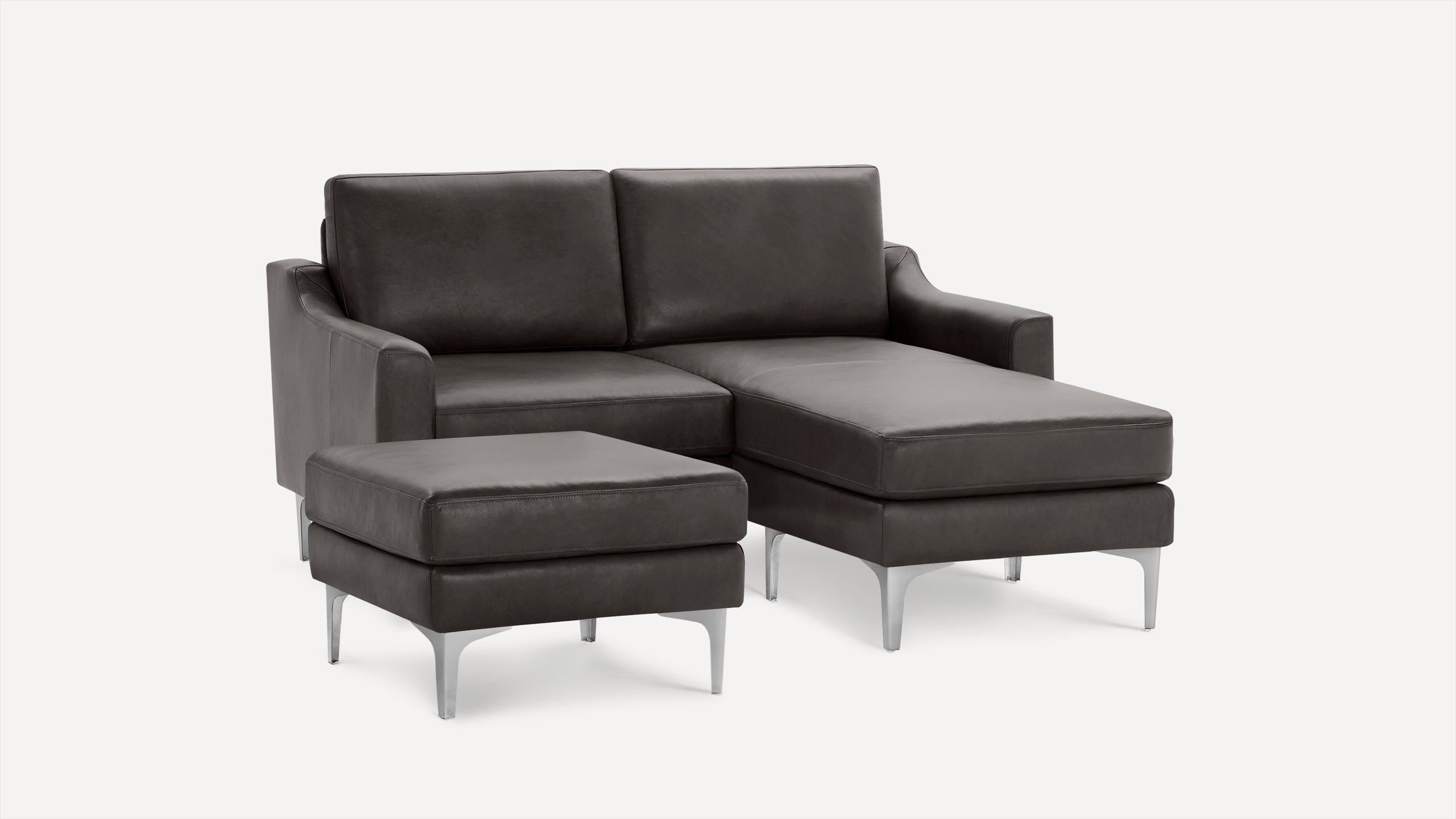 Modern dark gray leather sectional sofa with chaise lounge and matching ottoman, featuring sleek metal legs and clean lines.