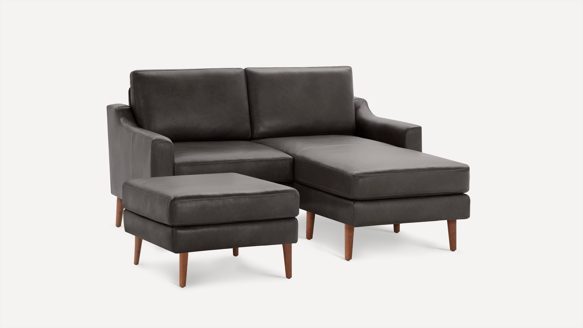 Dark gray leather sectional sofa with chaise lounge and matching ottoman, supported by wooden legs, modern design.