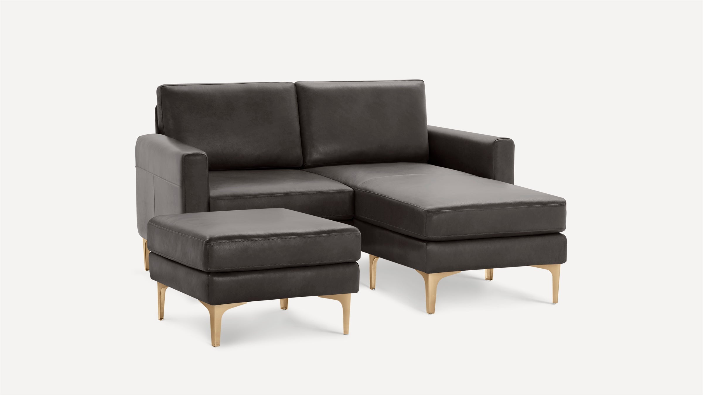 Dark gray leather sectional sofa with matching ottoman, gold-colored legs, modern design, and clean lines against a white background.