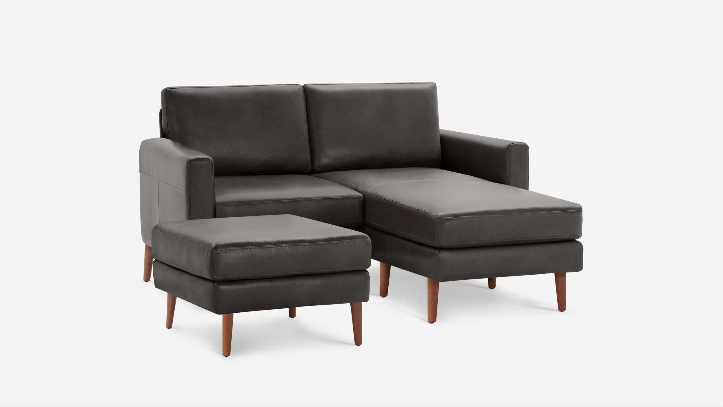 Dark gray leather sectional sofa with wooden legs and a matching ottoman against a plain white background.