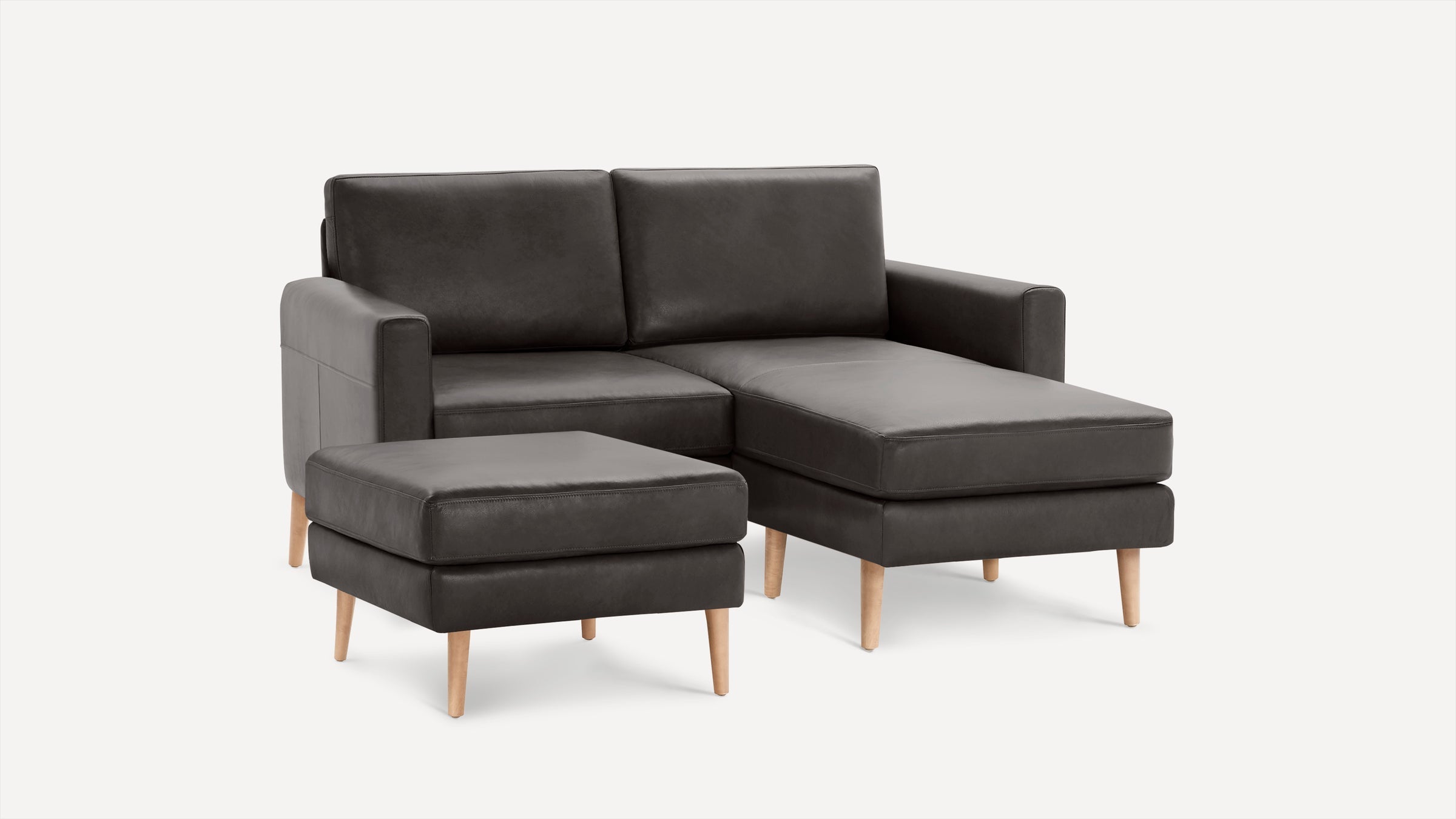 Dark gray leather sectional sofa with chaise lounge and matching ottoman on light wooden legs, modern minimalist design.