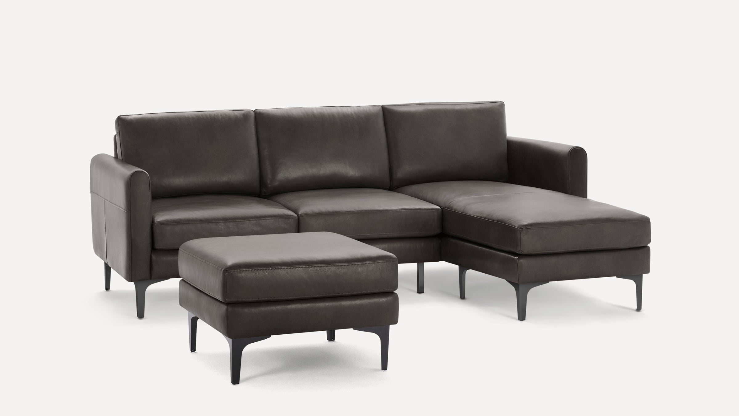 Dark gray leather sectional sofa with chaise lounge and matching ottoman, supported by sleek black metal legs.
