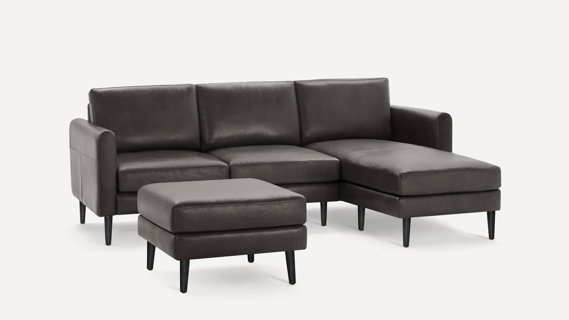 Dark gray leather sectional sofa with chaise and matching ottoman, featuring sleek, tapered black legs and modern design.