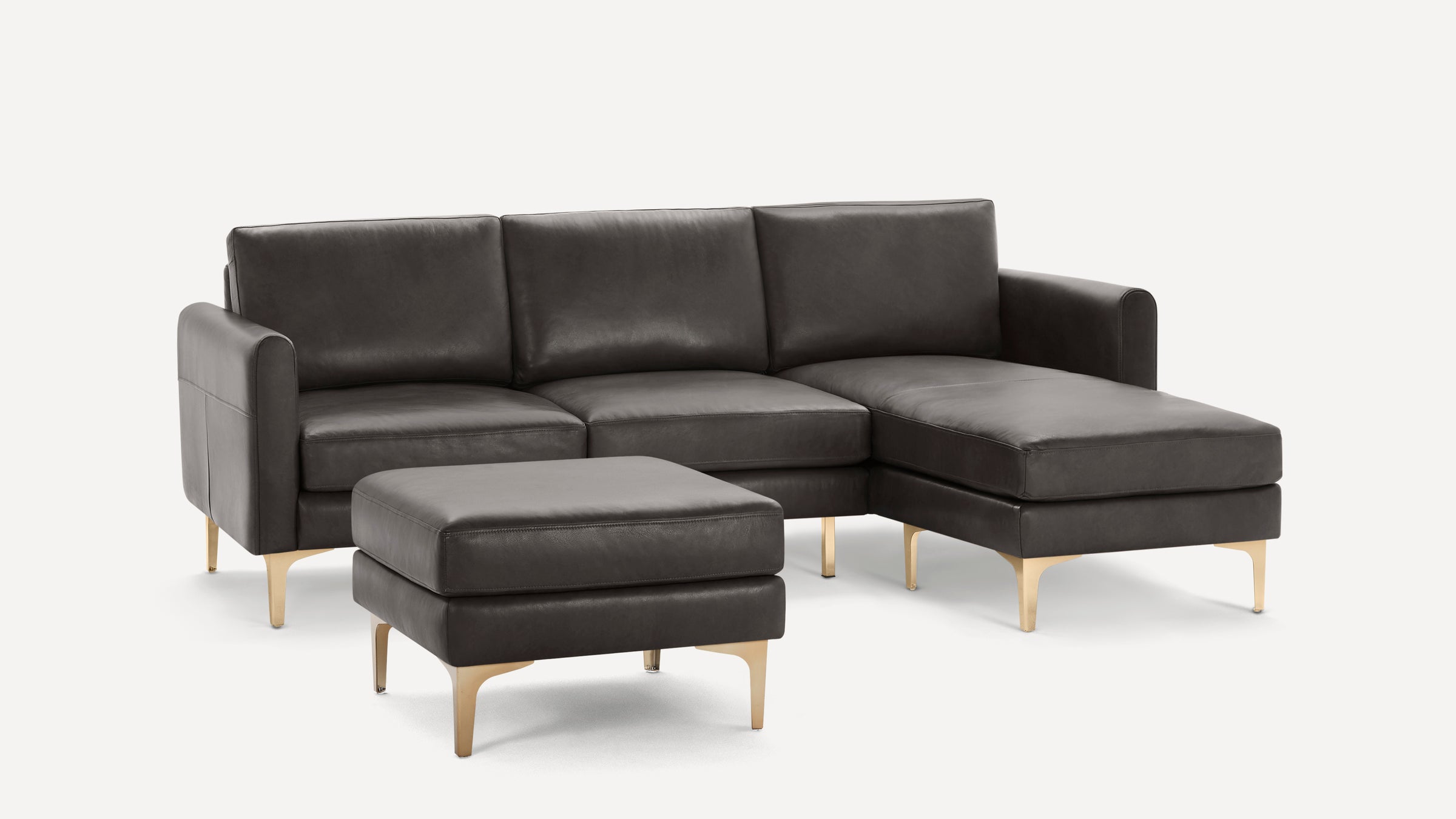 Dark gray leather sectional sofa with matching ottoman, featuring sleek gold metal legs and modern design.