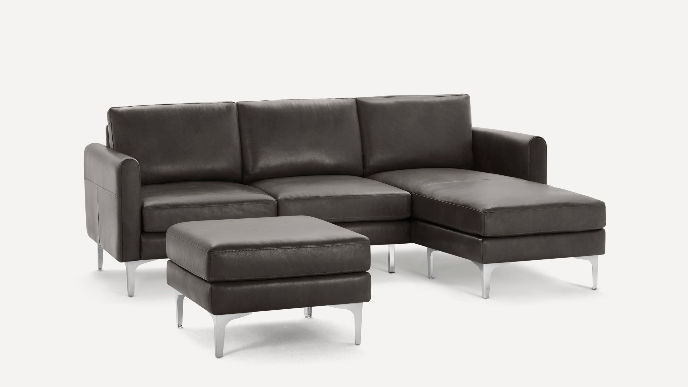 Modern dark gray sectional leather sofa with chaise lounge and matching ottoman, featuring sleek metal legs.