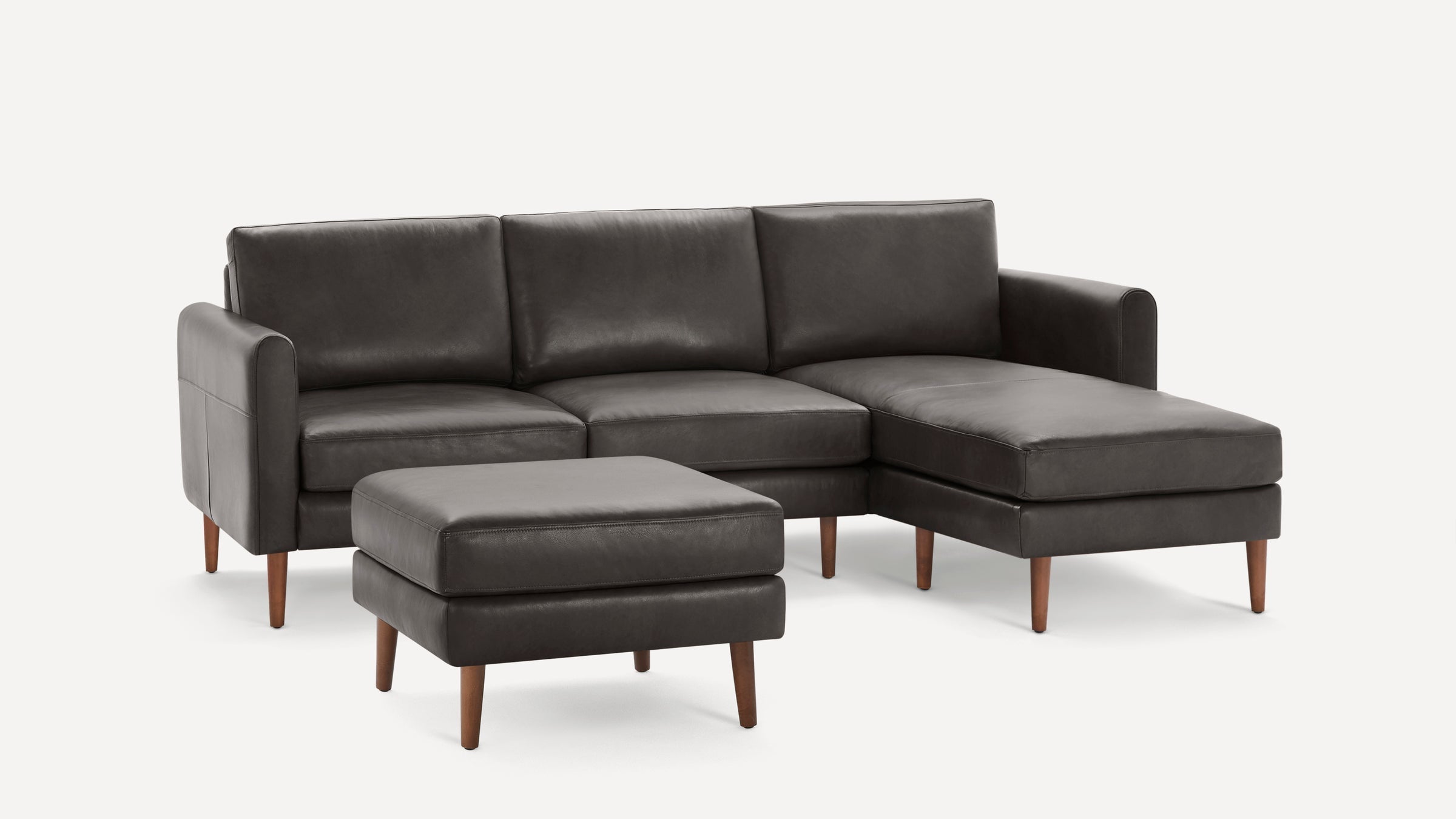 Modern dark gray leather sectional sofa with matching ottoman, wooden legs, clean lines, and cushioned seats and backrests.