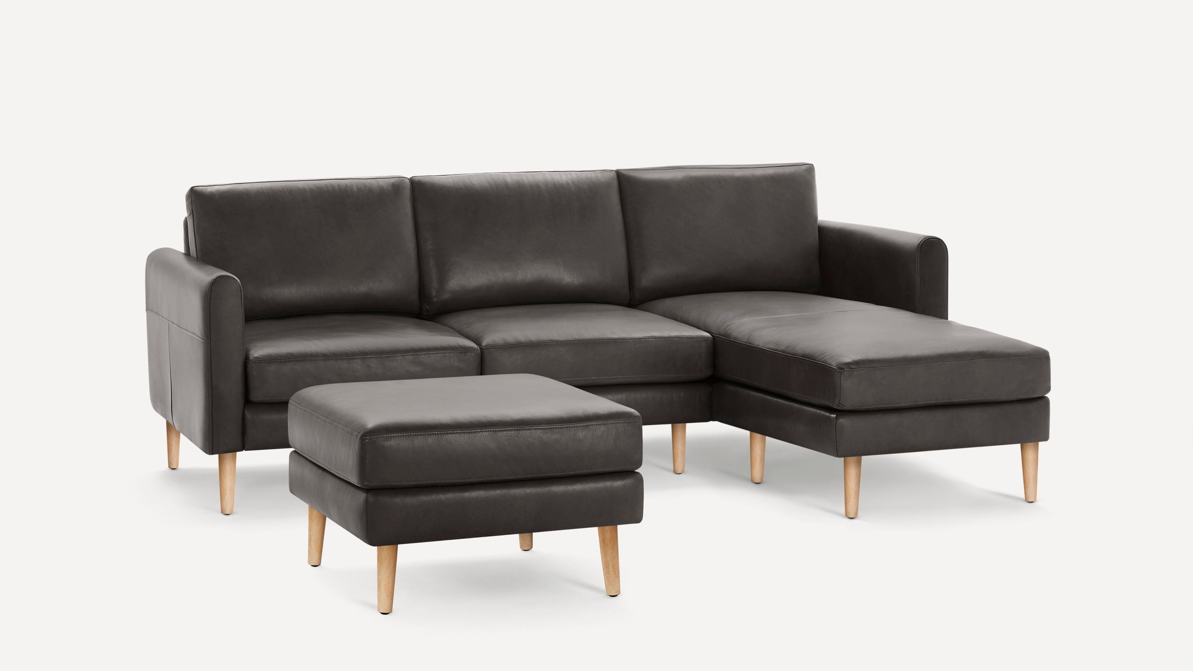 Dark gray leather sectional sofa with matching ottoman, wooden legs, clean modern design, three-seat cushions, and chaise lounge on the right side.