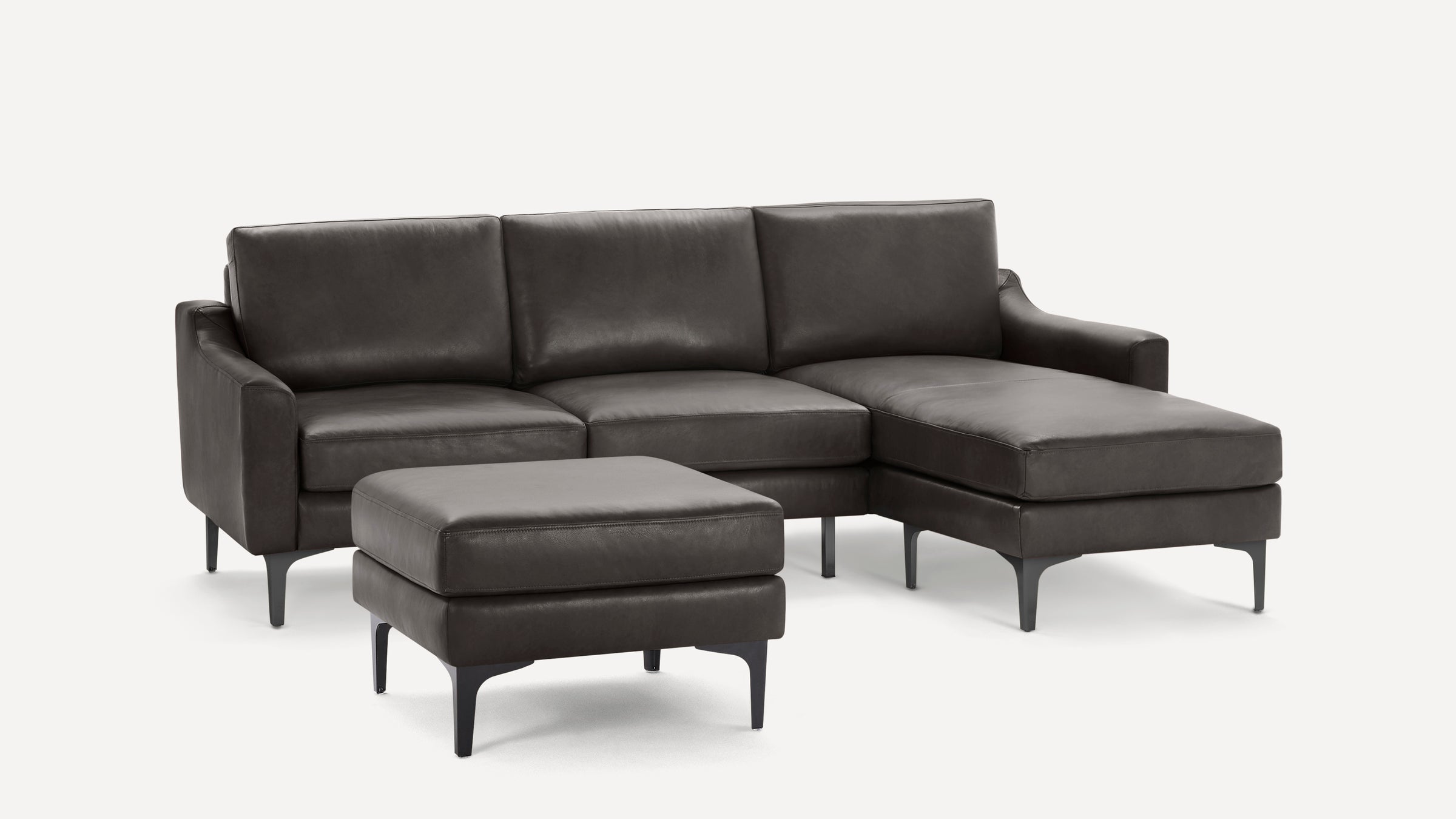 Dark gray modern leather sectional sofa with chaise lounge and matching ottoman, featuring slim black legs.