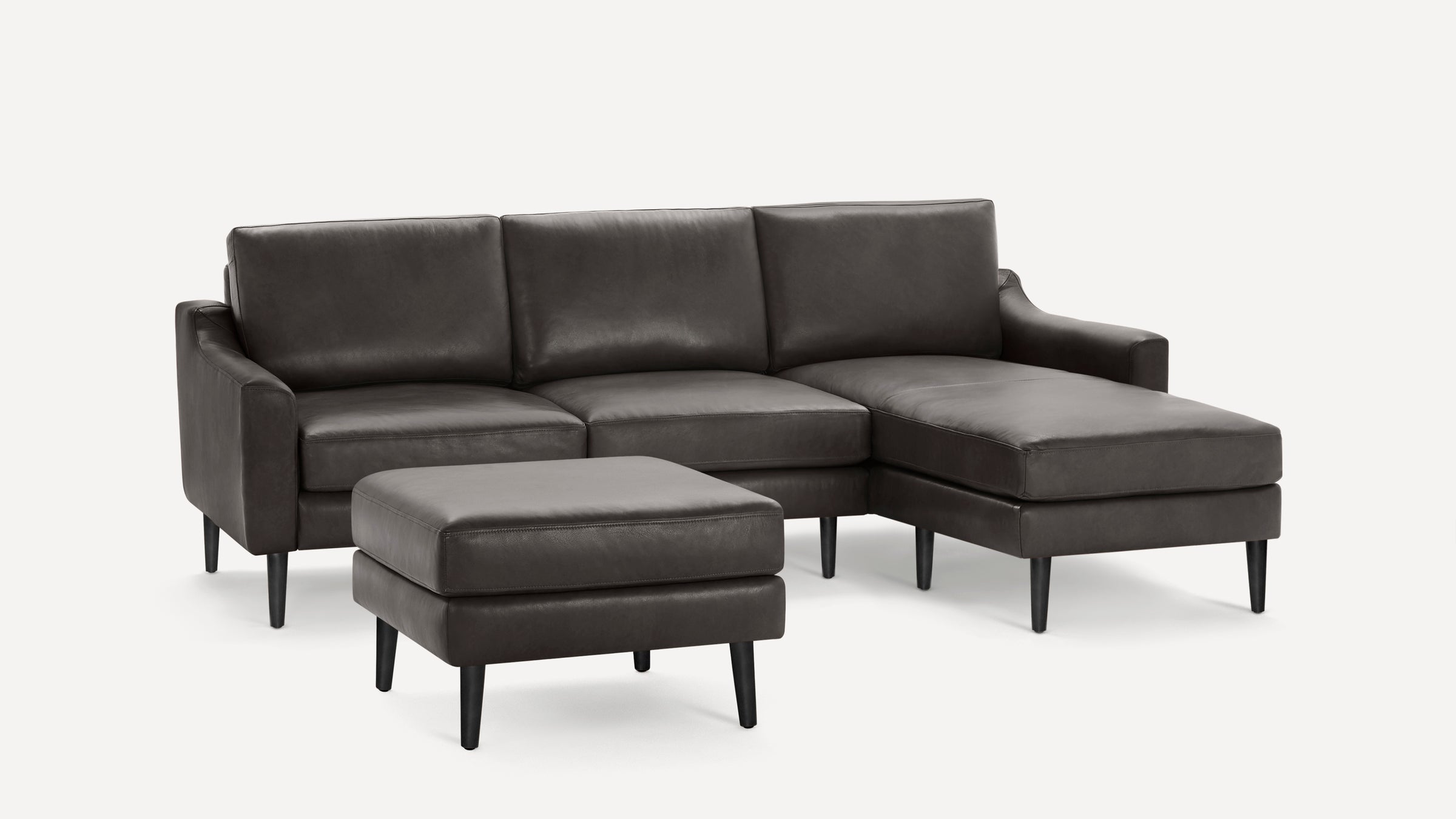 Modern dark gray leather sectional sofa with chaise lounge and matching ottoman, supported by black tapered legs.
