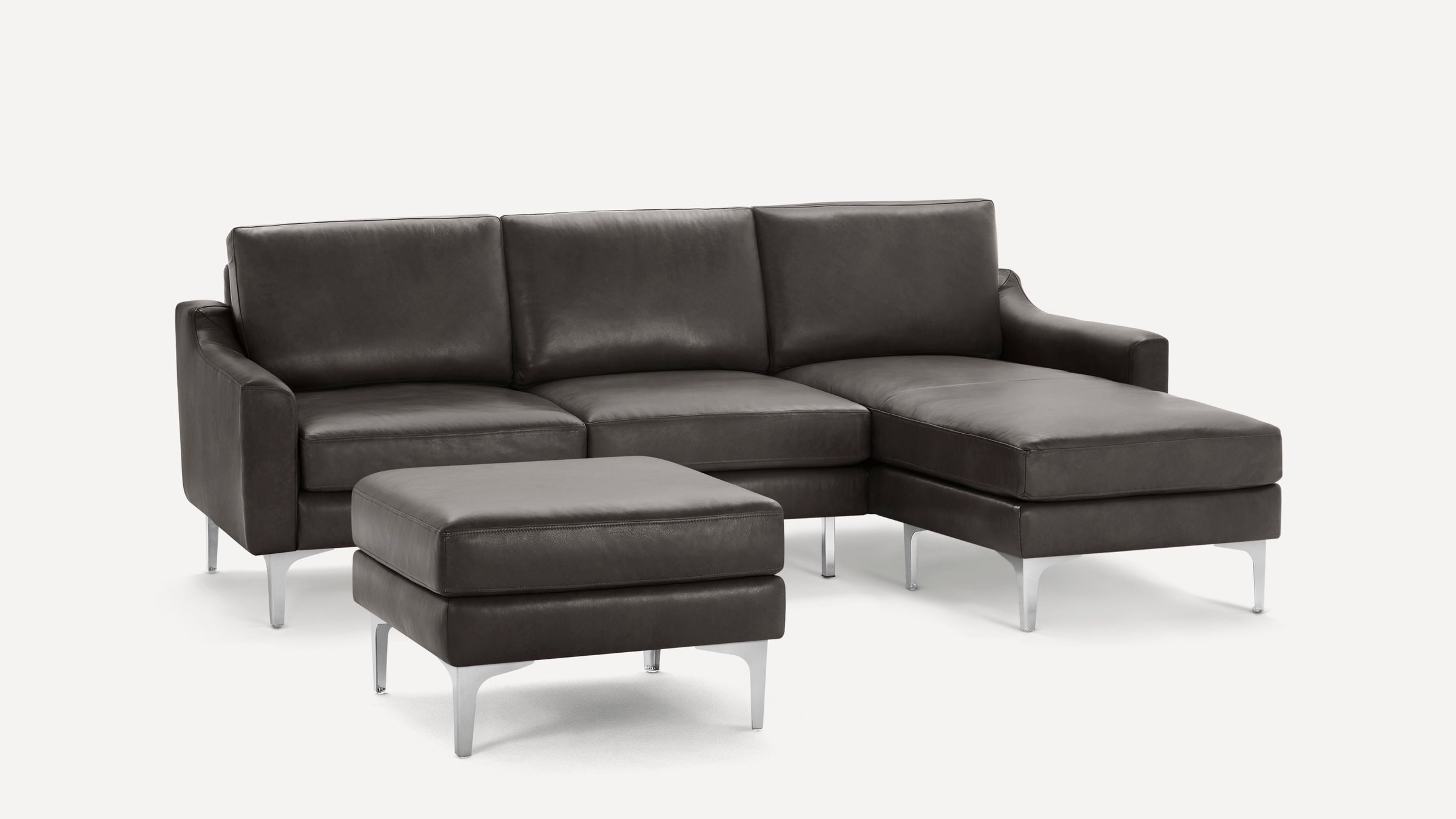 Modern dark gray leather sectional sofa with chaise lounge on the right and a matching ottoman, all supported by sleek metal legs.
