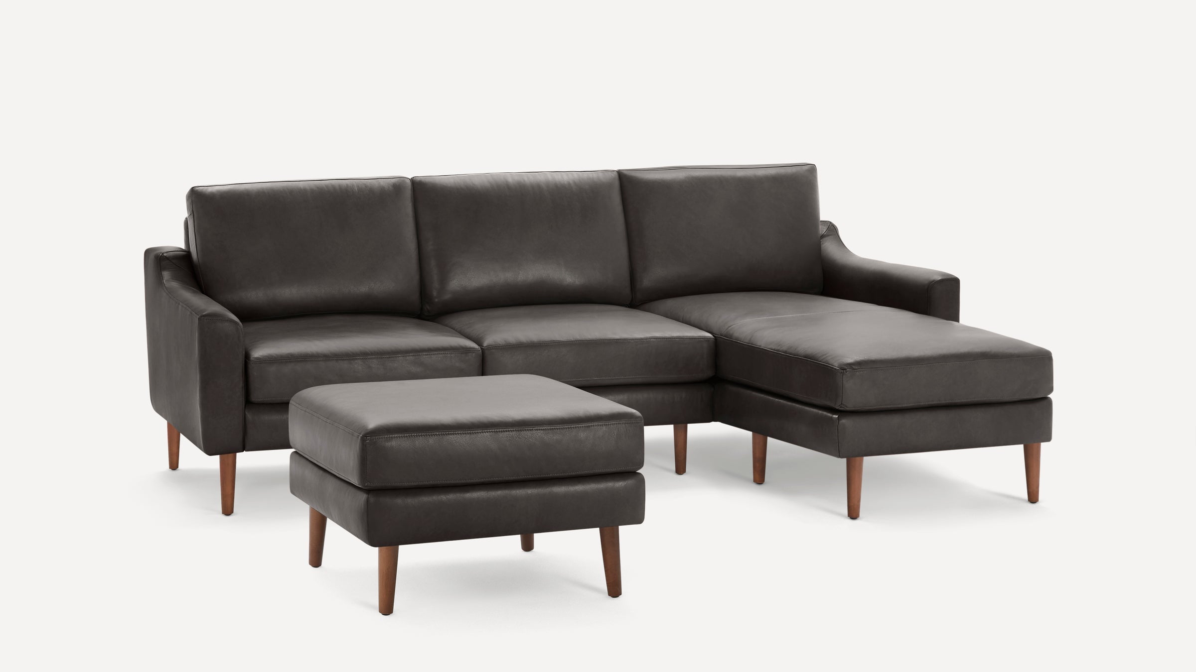 Dark gray leather sectional sofa with chaise lounge and matching ottoman, featuring wooden tapered legs in mid-century modern style.
