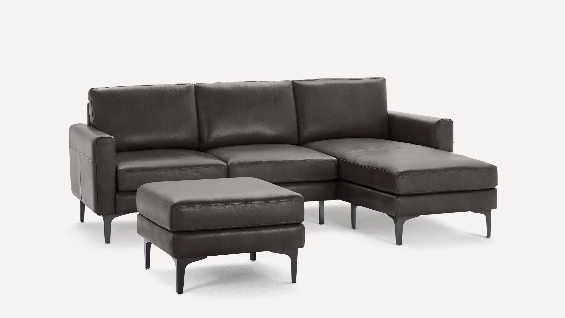 Modern dark gray leather sectional sofa with chaise lounge and matching ottoman, featuring sleek black metal legs.
