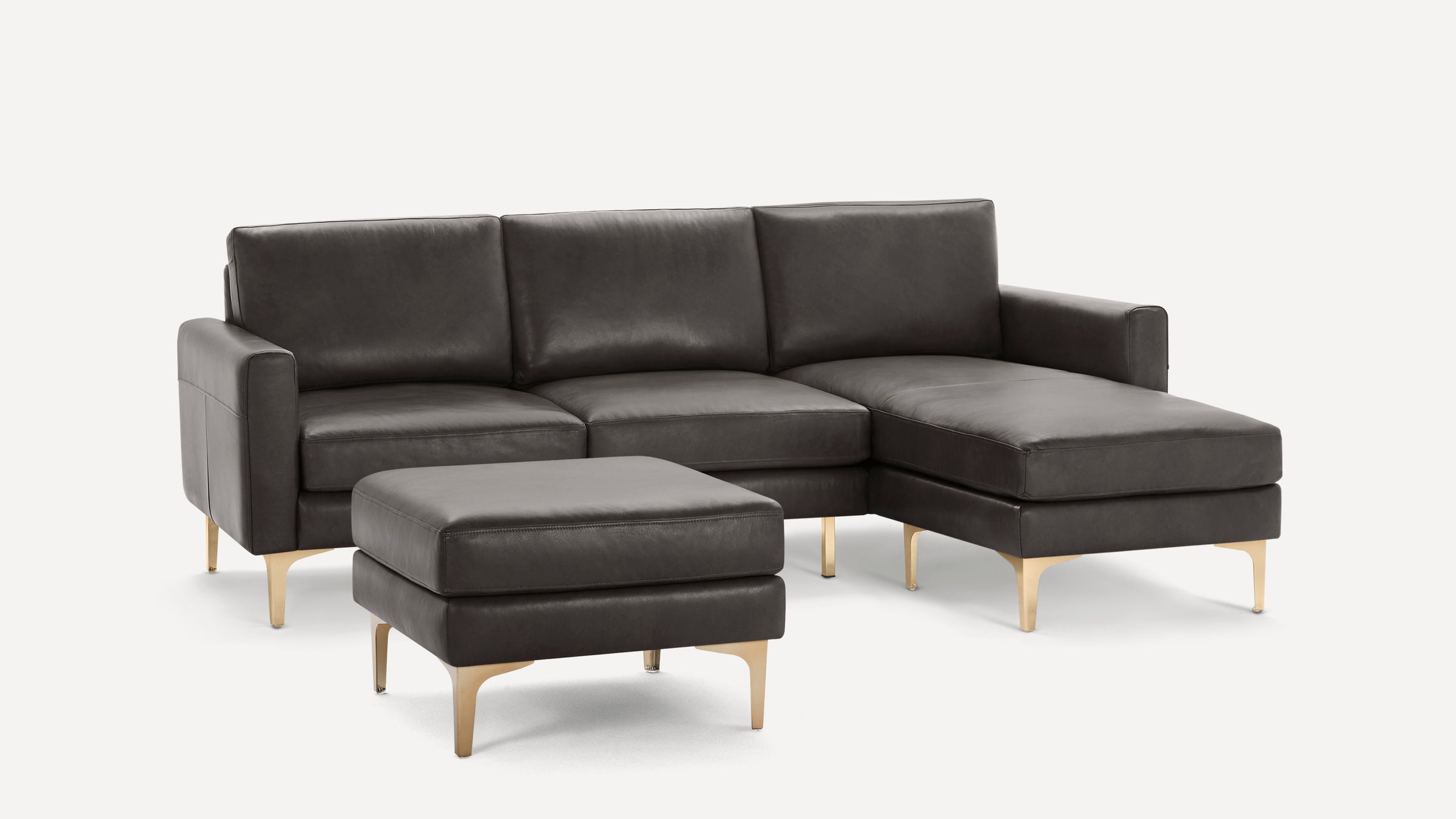 Modern dark gray leather sectional sofa with chaise lounge and matching ottoman, featuring sleek gold metal legs.