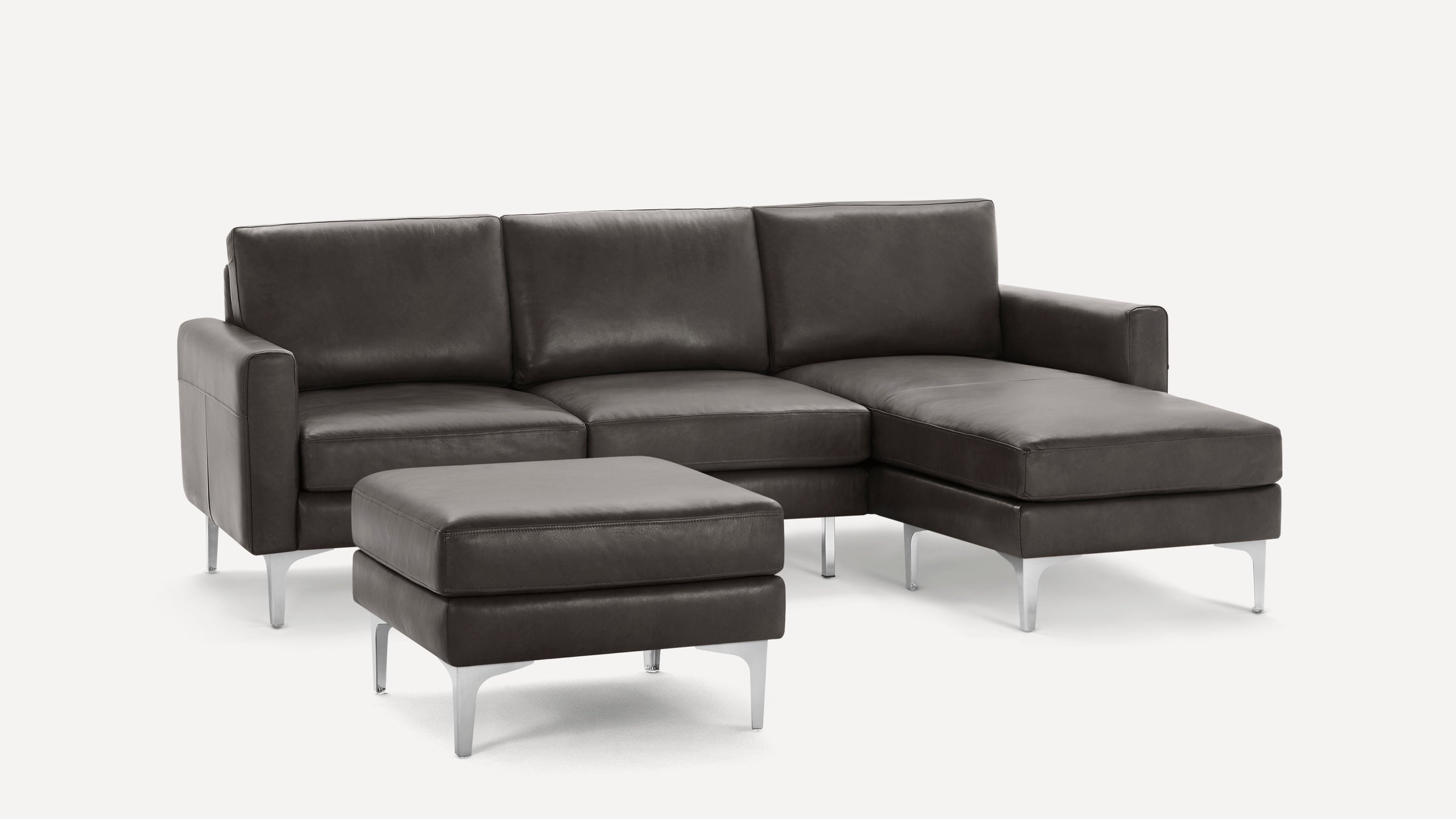 Modern dark gray leather sectional sofa with chrome legs and matching ottoman on a white background.