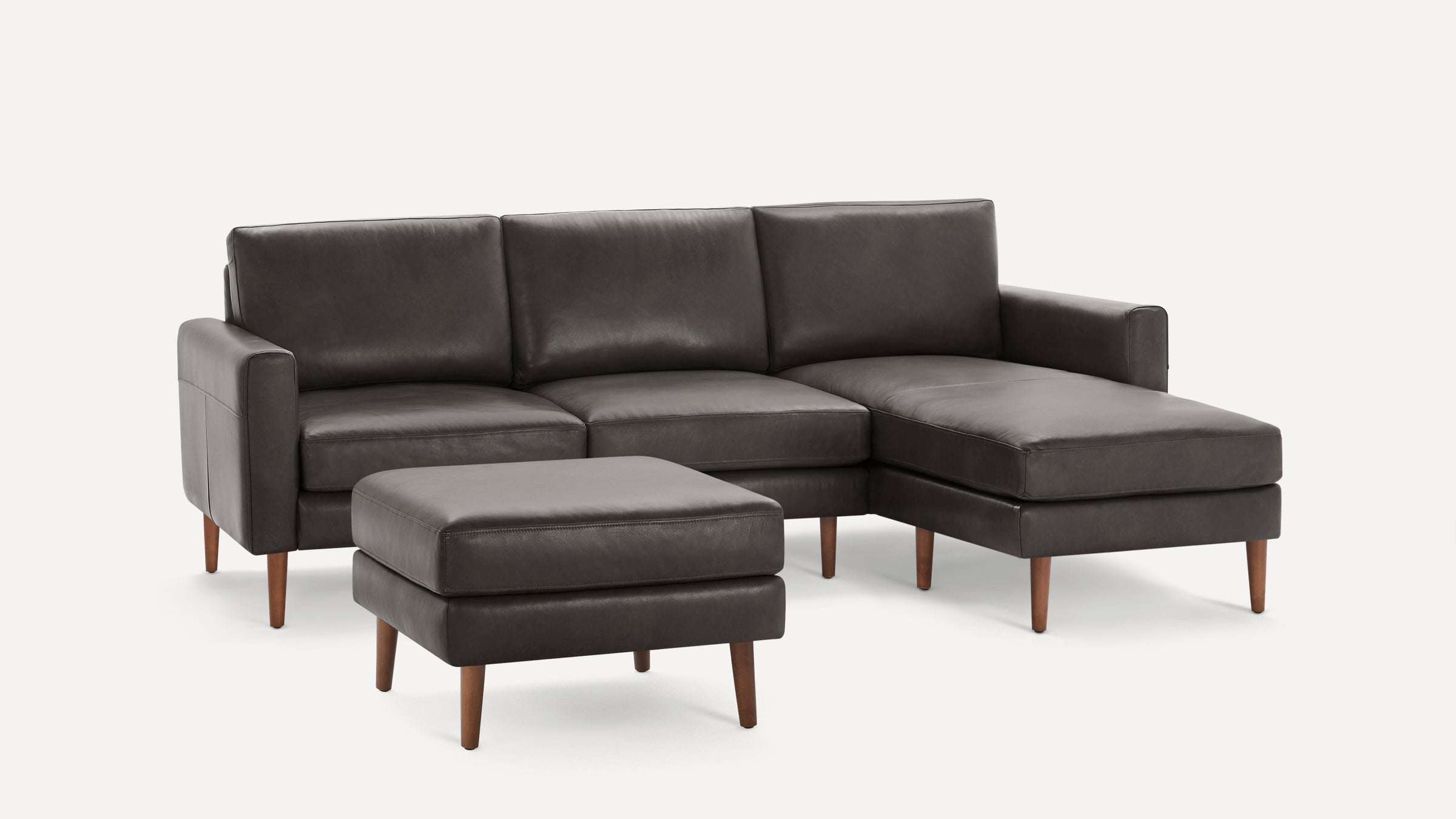 Dark gray leather sectional sofa with wooden legs, featuring three back cushions and a matching ottoman.