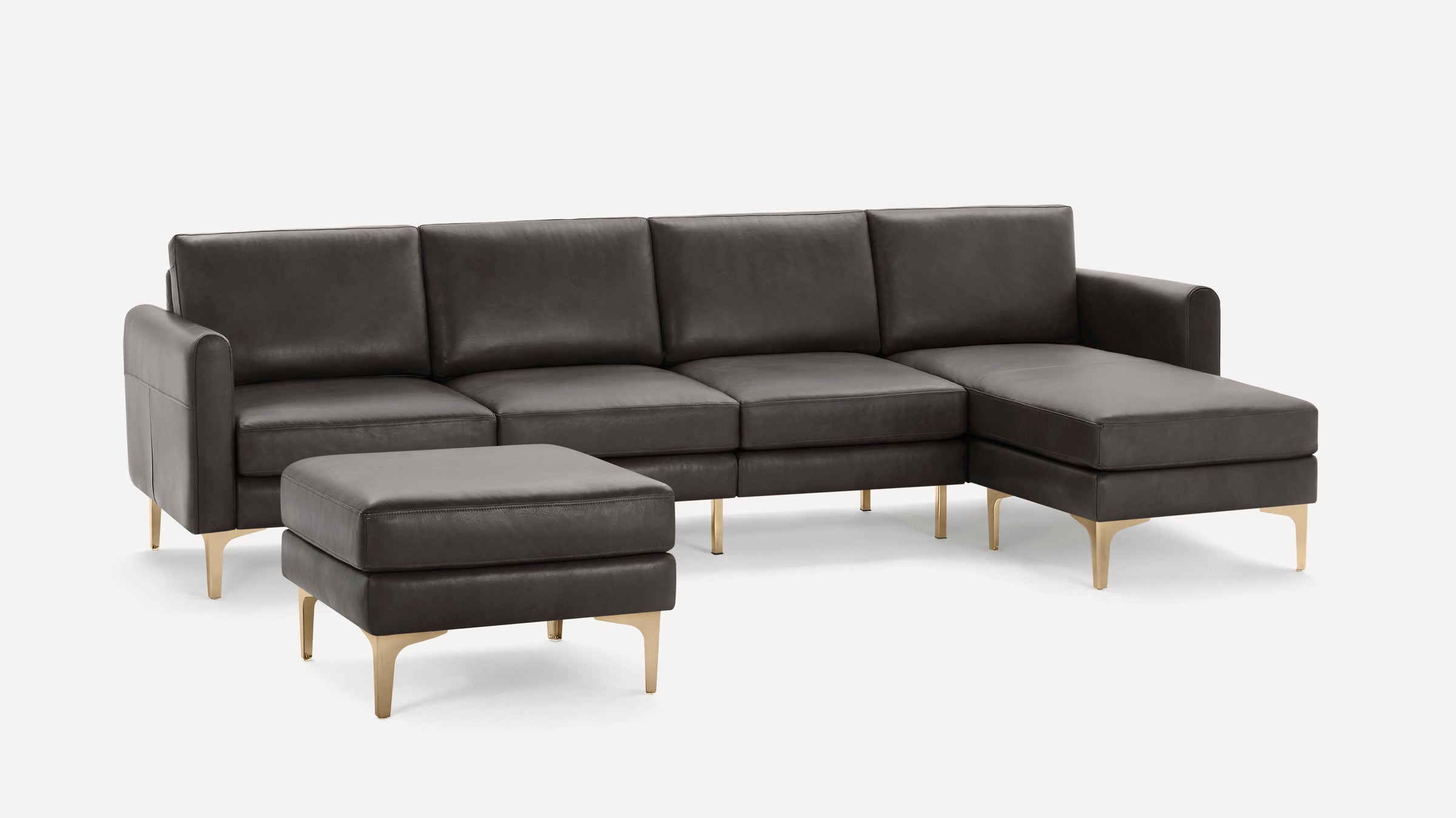 Dark grey leather sectional sofa with gold metal legs, featuring a chaise lounge and matching ottoman on white background.