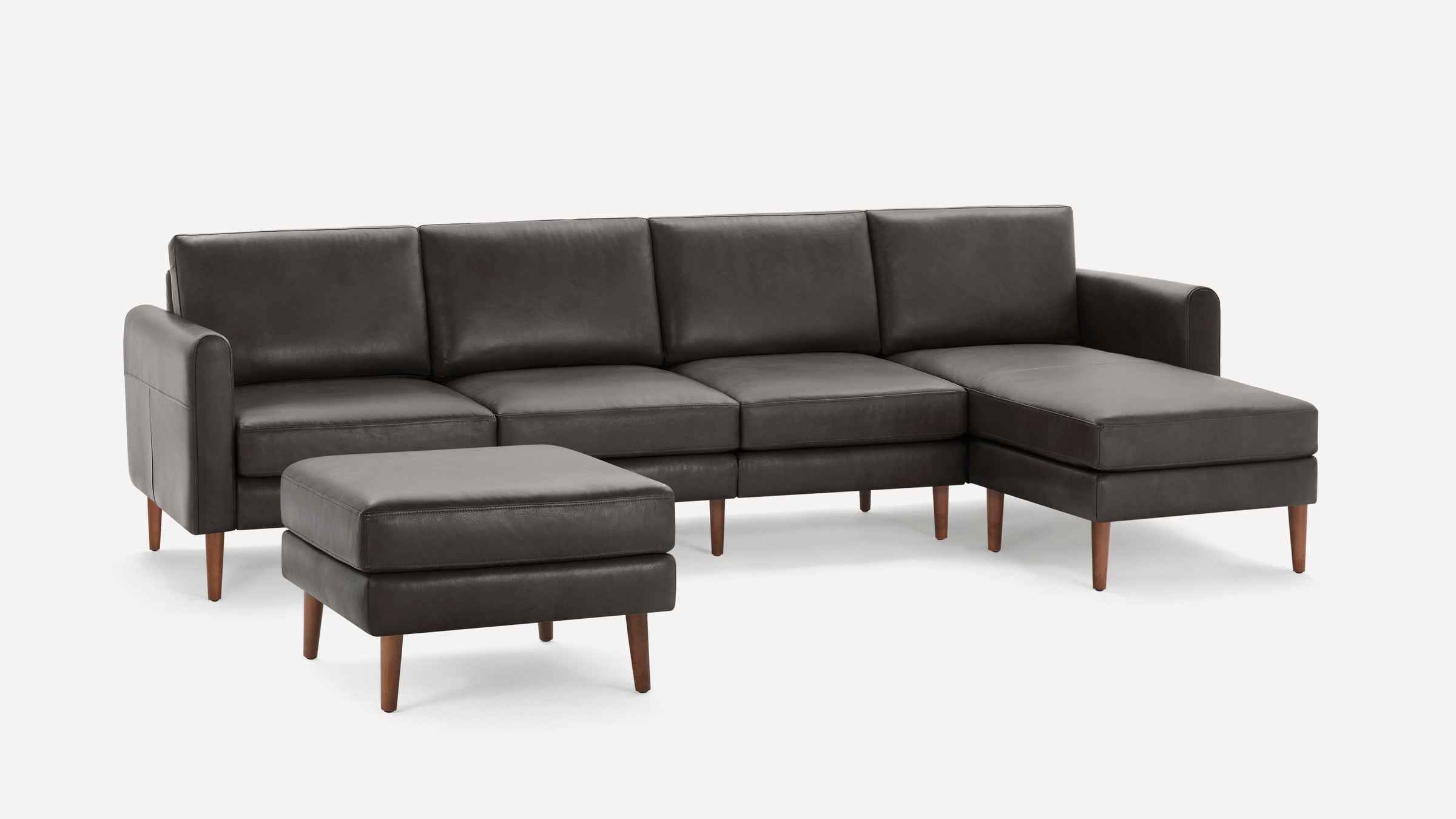 Modern dark gray sectional sofa with chaise lounge and matching ottoman, featuring wooden tapered legs and smooth leather upholstery.