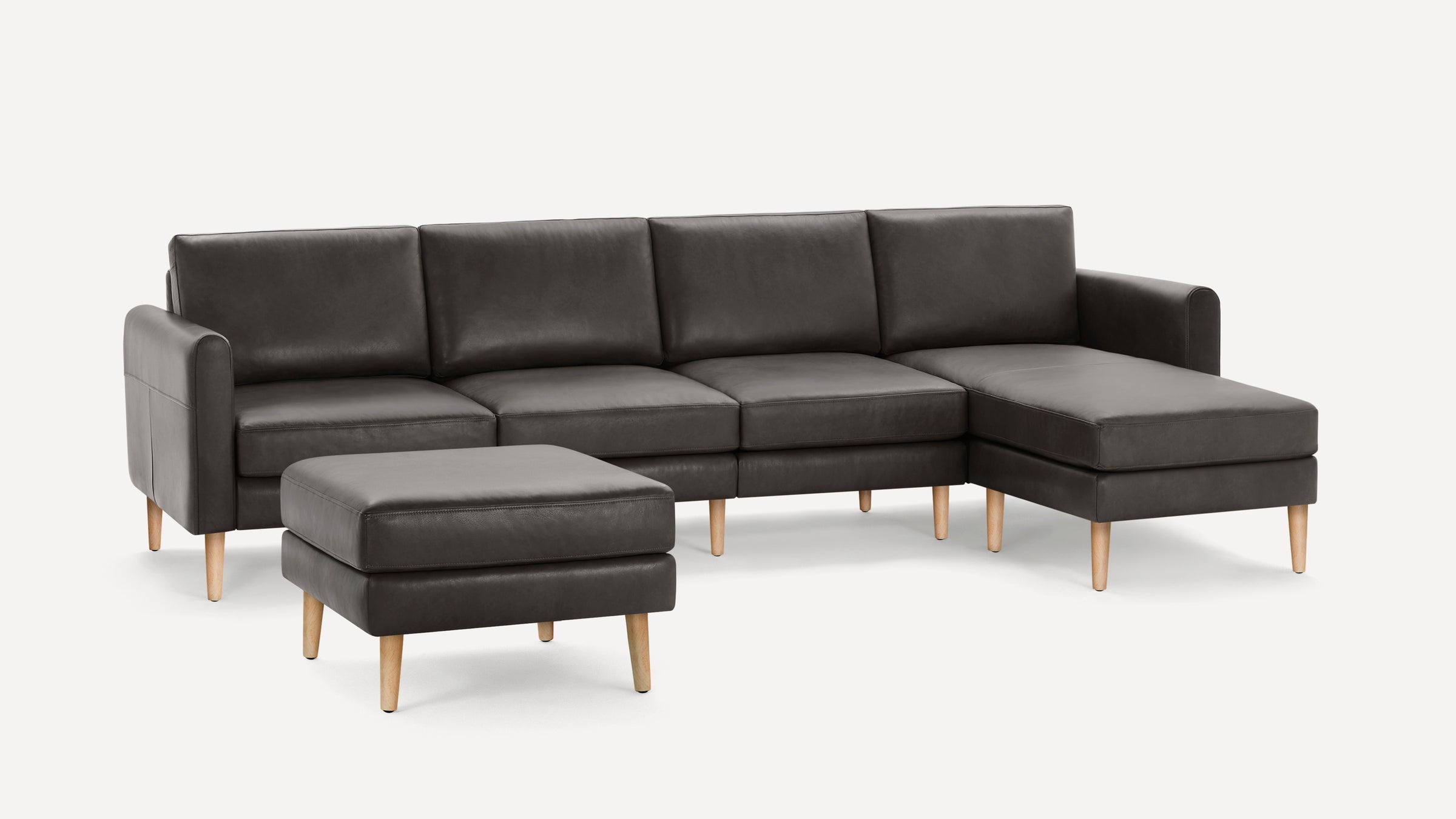Modern dark gray leather sectional sofa with light wooden legs and matching ottoman, clean lines, and plush cushions.