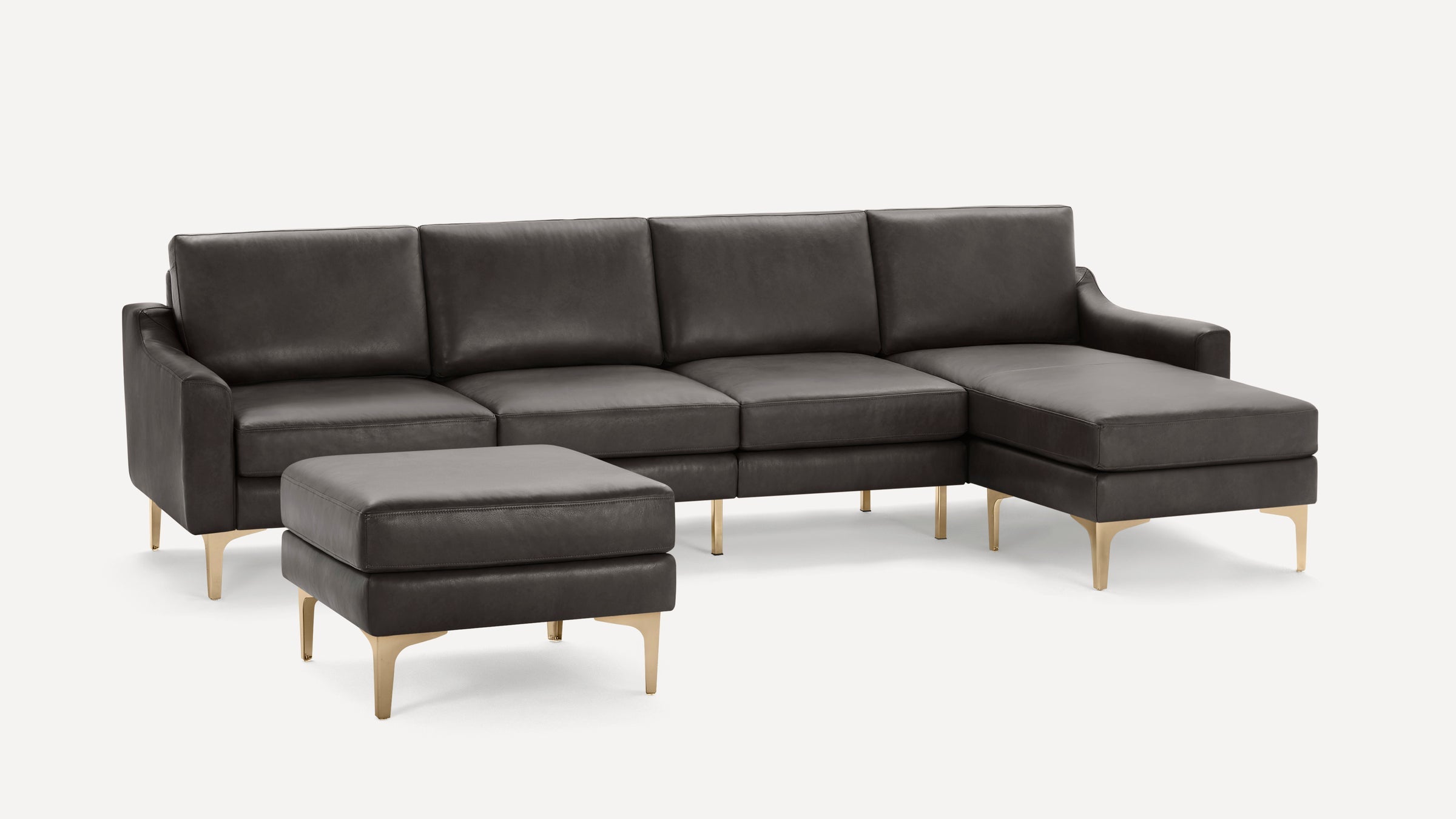 Dark gray leather sectional sofa with matching ottoman, angled armrests, and gold metallic legs on white background.