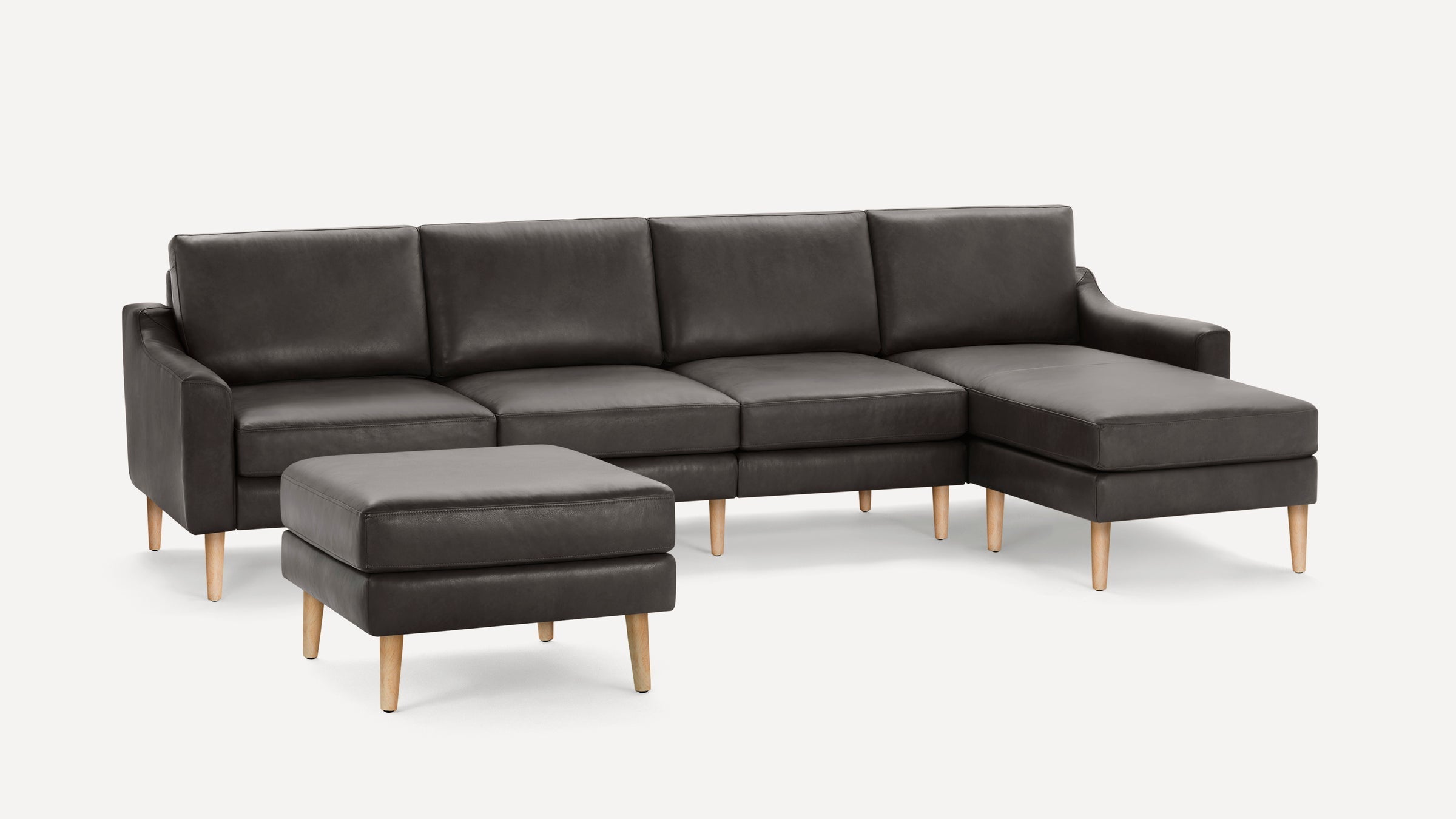 Dark gray leather sectional sofa with wooden legs, including a chaise and a matching ottoman on a white background.