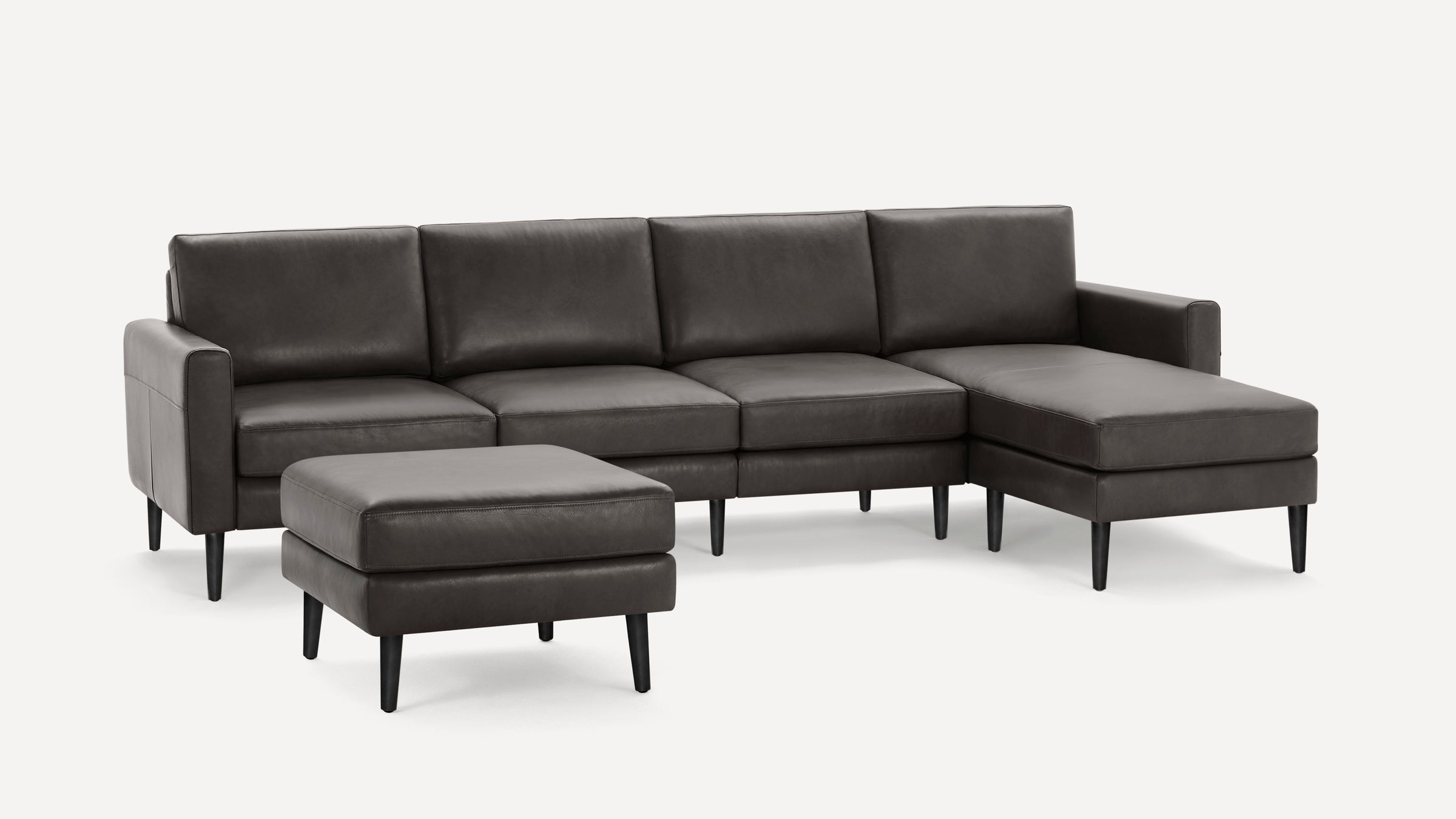 Dark gray leather sectional sofa with chaise lounge and matching ottoman, featuring sleek black tapered legs.