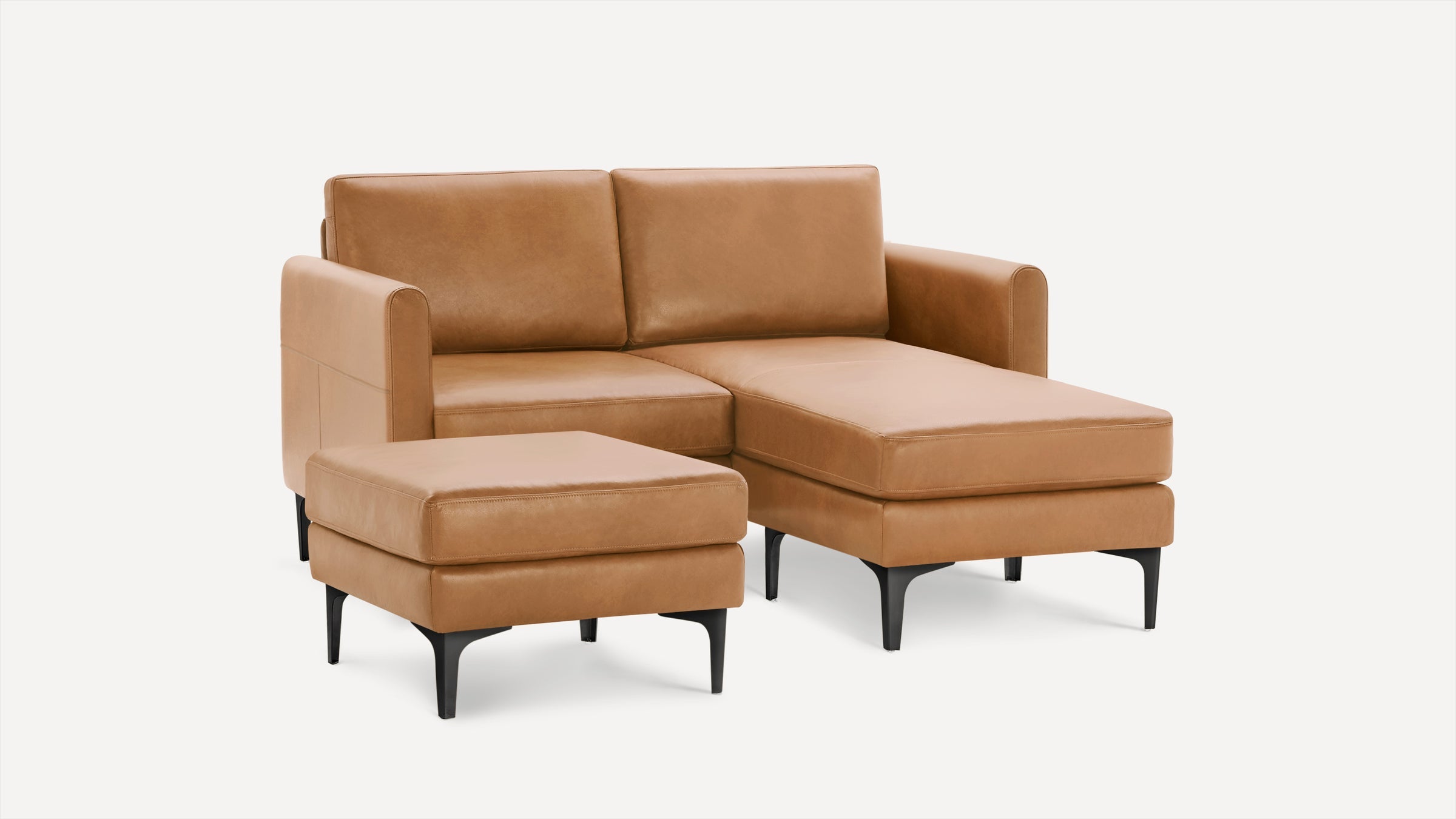 Tan leather sectional sofa with chaise lounge and matching ottoman on black legs, modern design against white background.