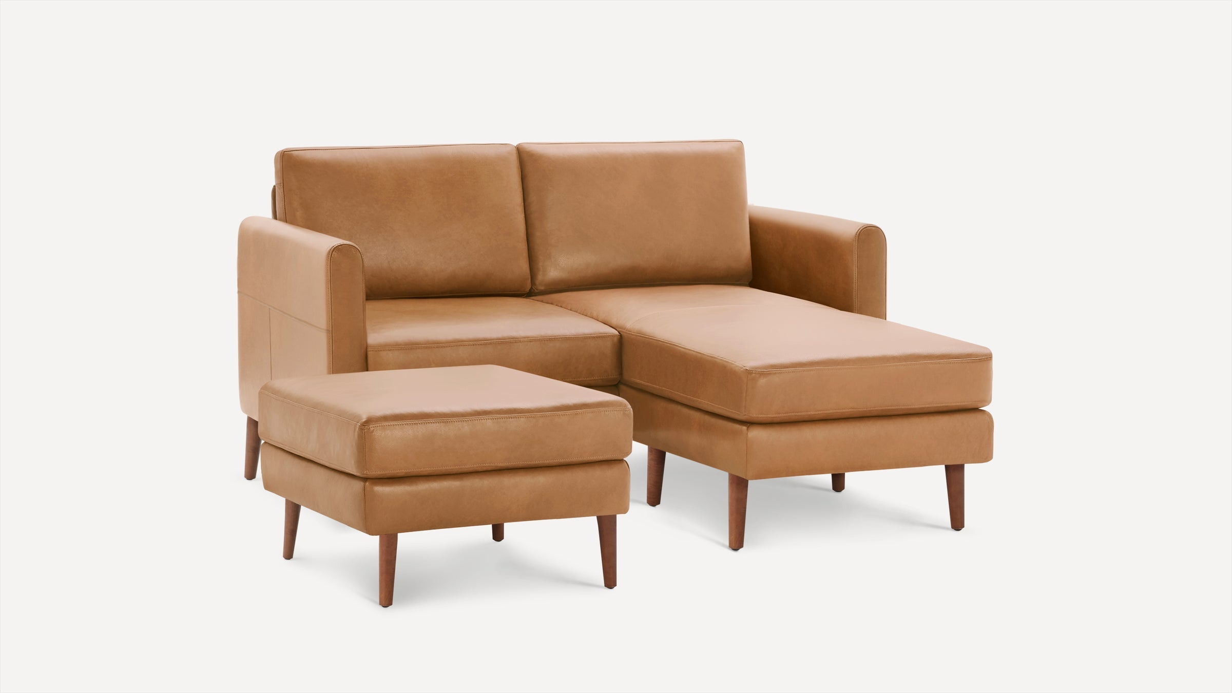 Tan leather sectional sofa with chaise lounge and matching ottoman, supported by tapered wooden legs.