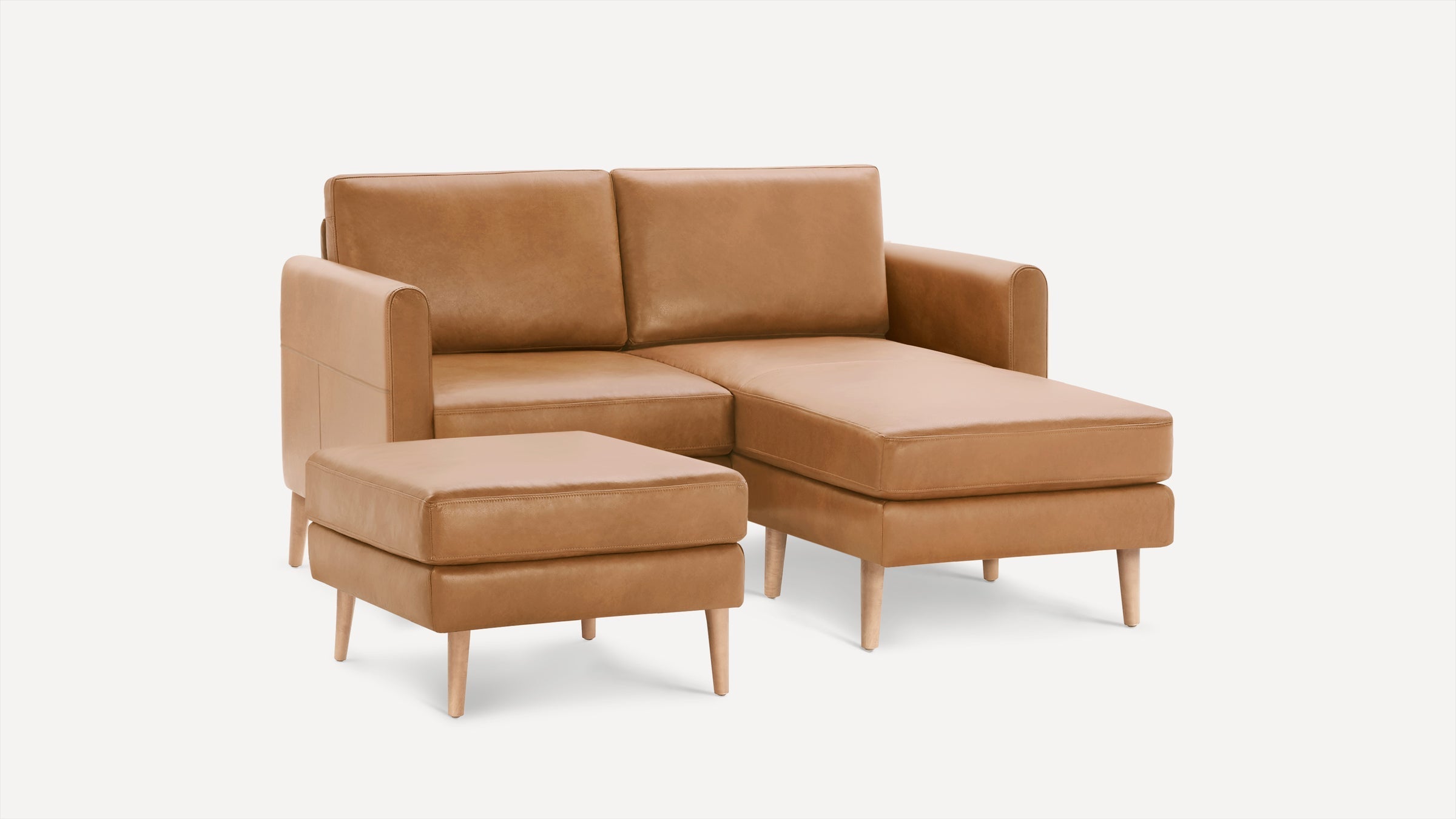 Tan leather sectional sofa with chaise lounge and matching ottoman, featuring wooden legs and modern design.